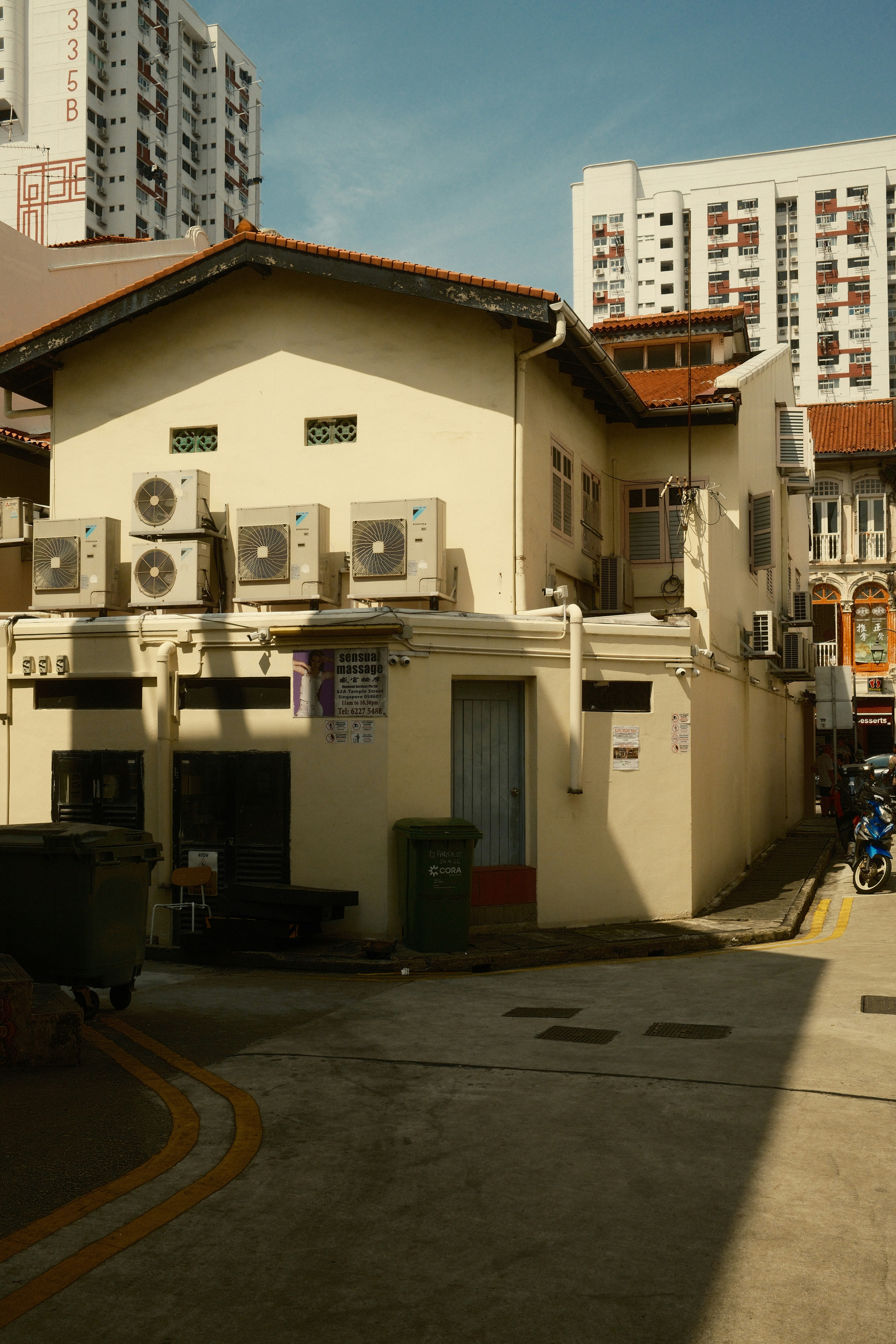 A cream-colored building with air conditioning units in a narrow urban alleyway.