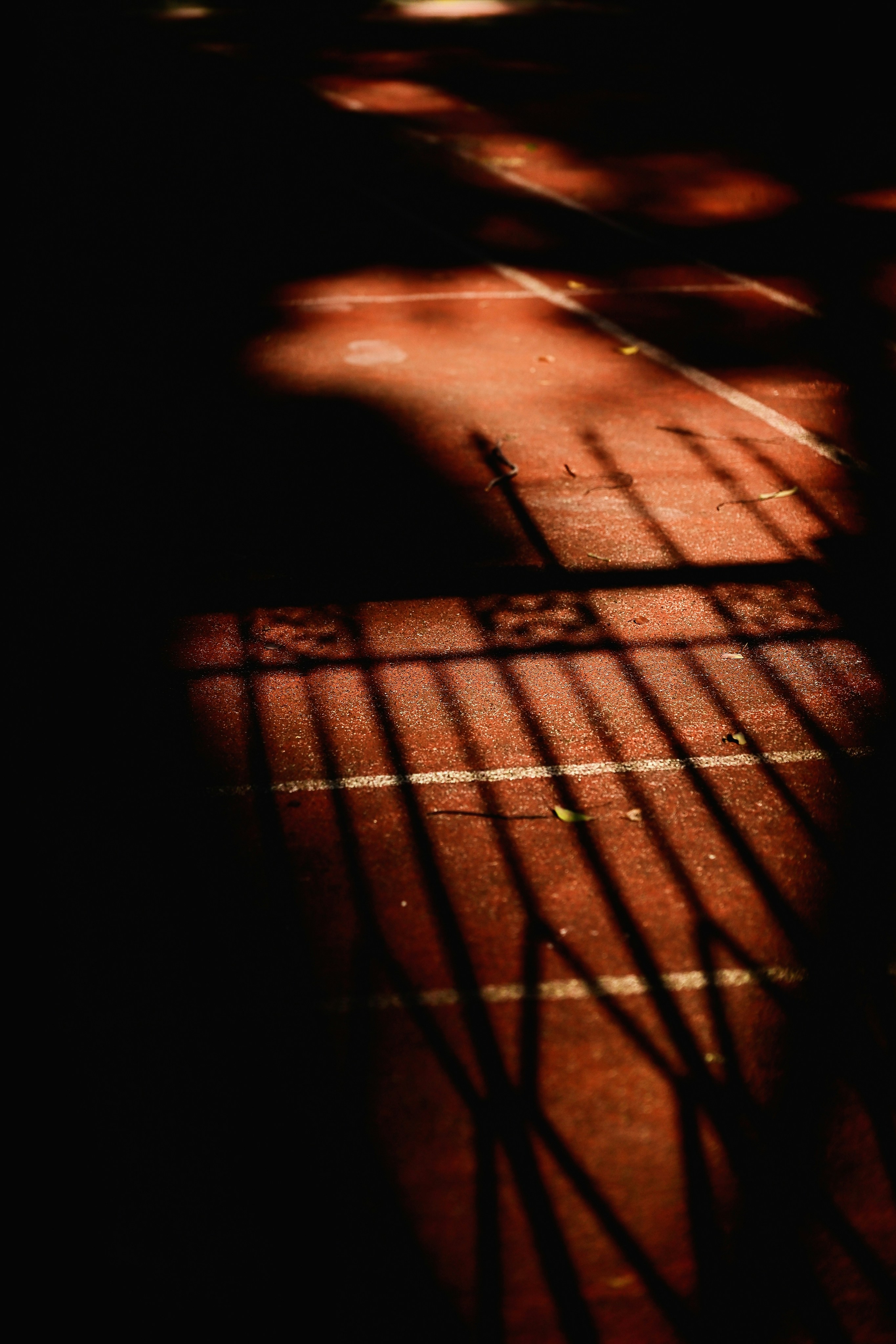 A red running track surface with long shadows cast by a metal fence