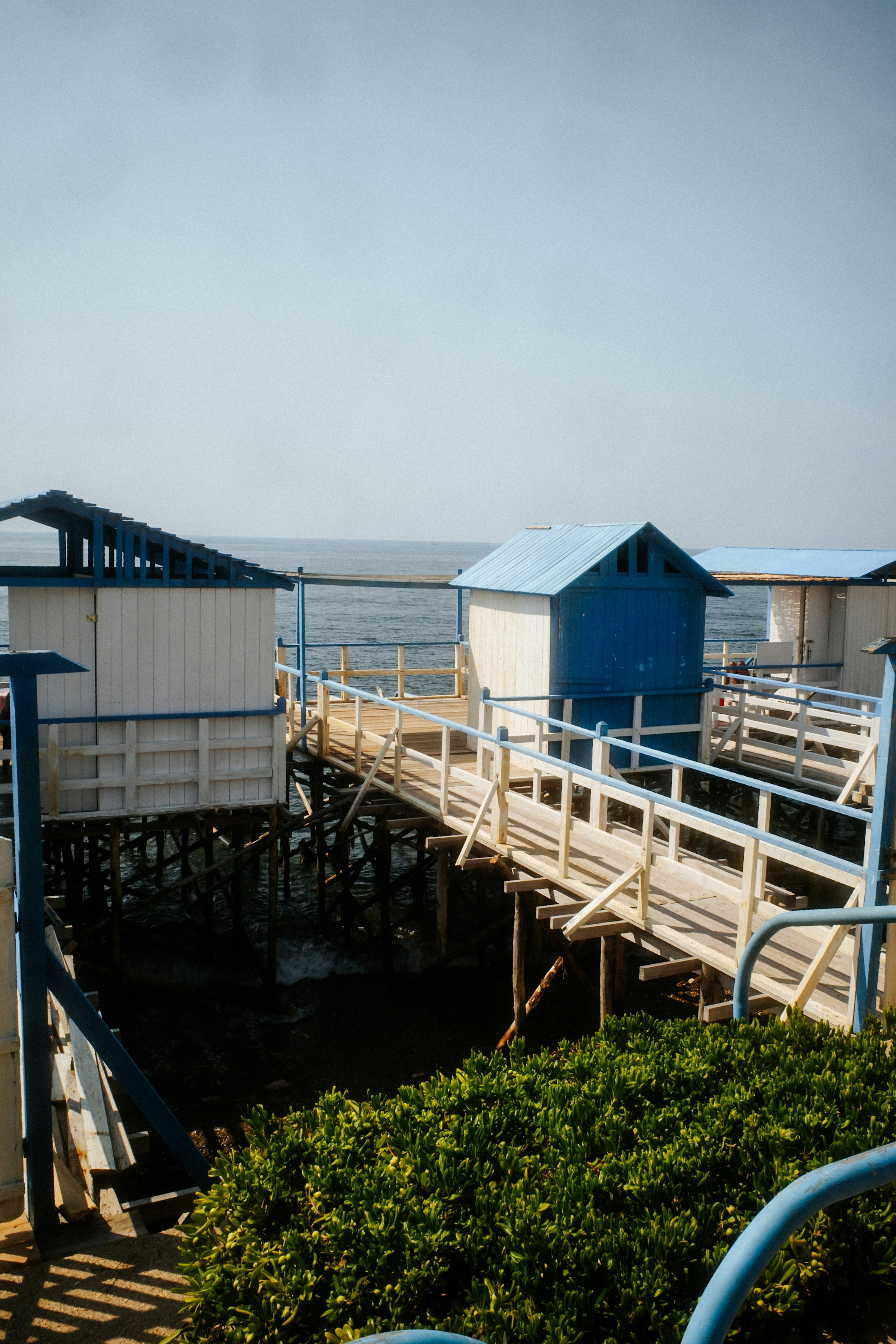 Small blue and white wooden cabins on a pier over the ocean.