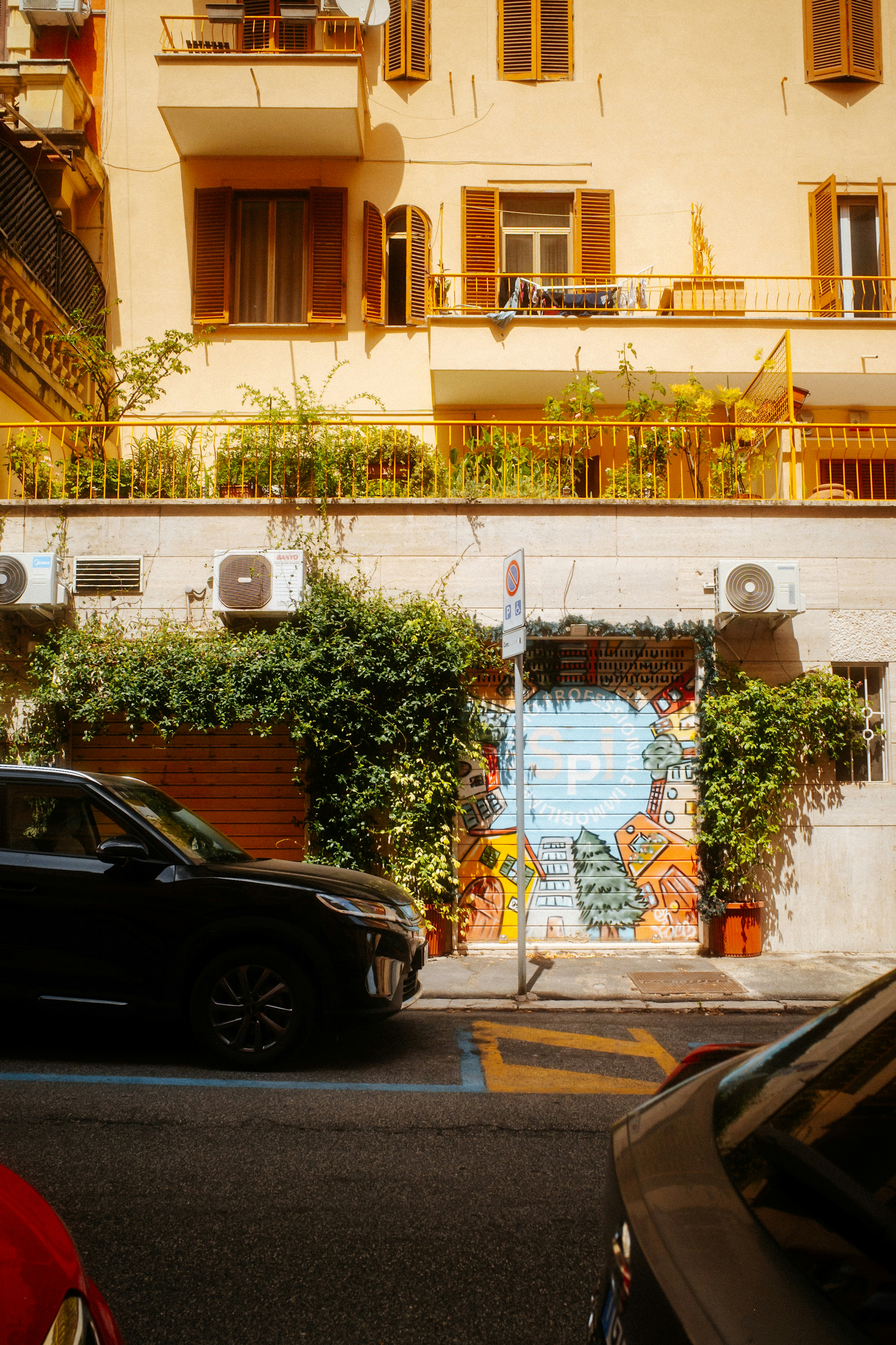 A black car parked on a street before a building with a mural.