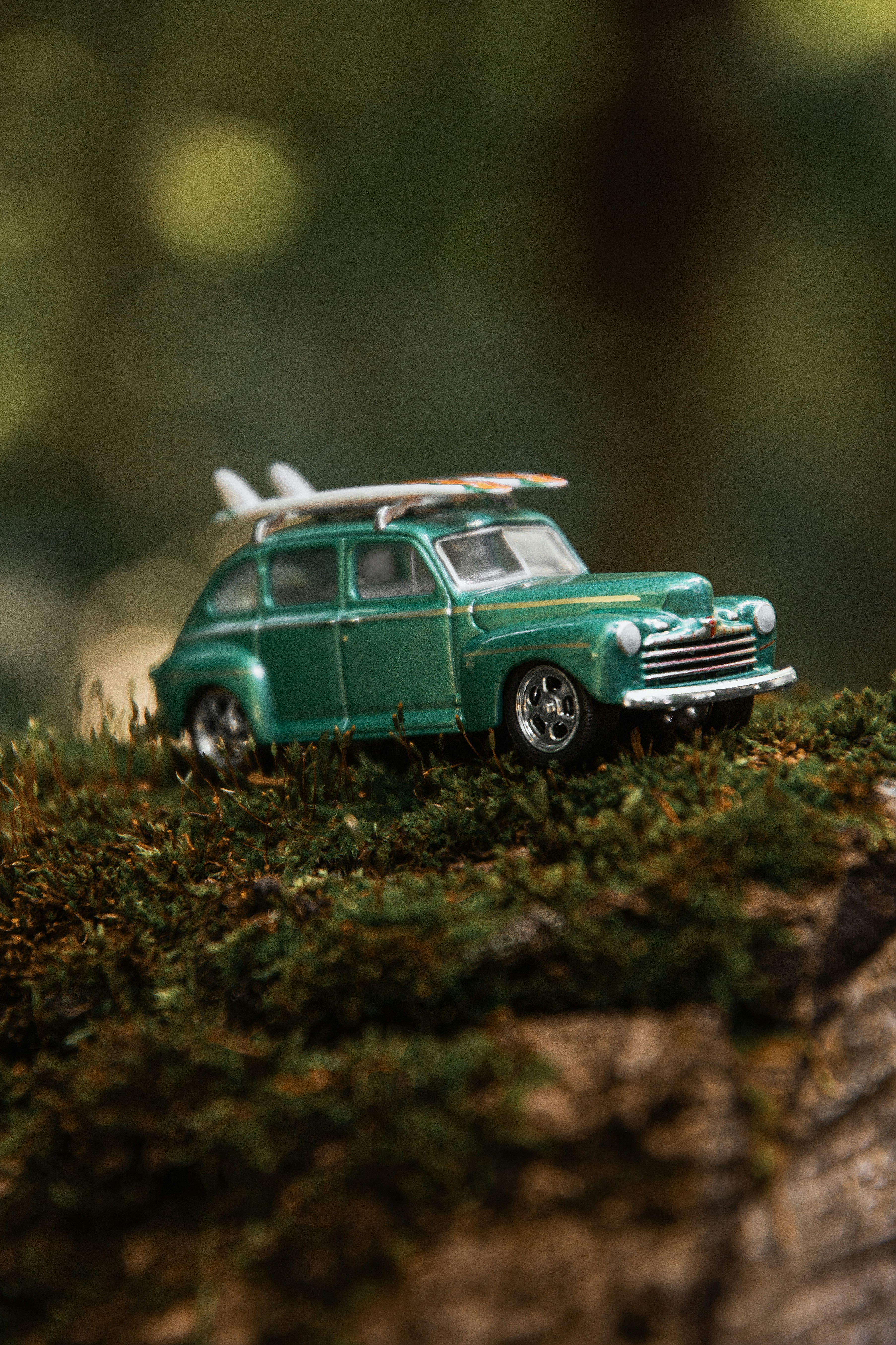 A green toy car with surfboards on its roof on a mossy log.