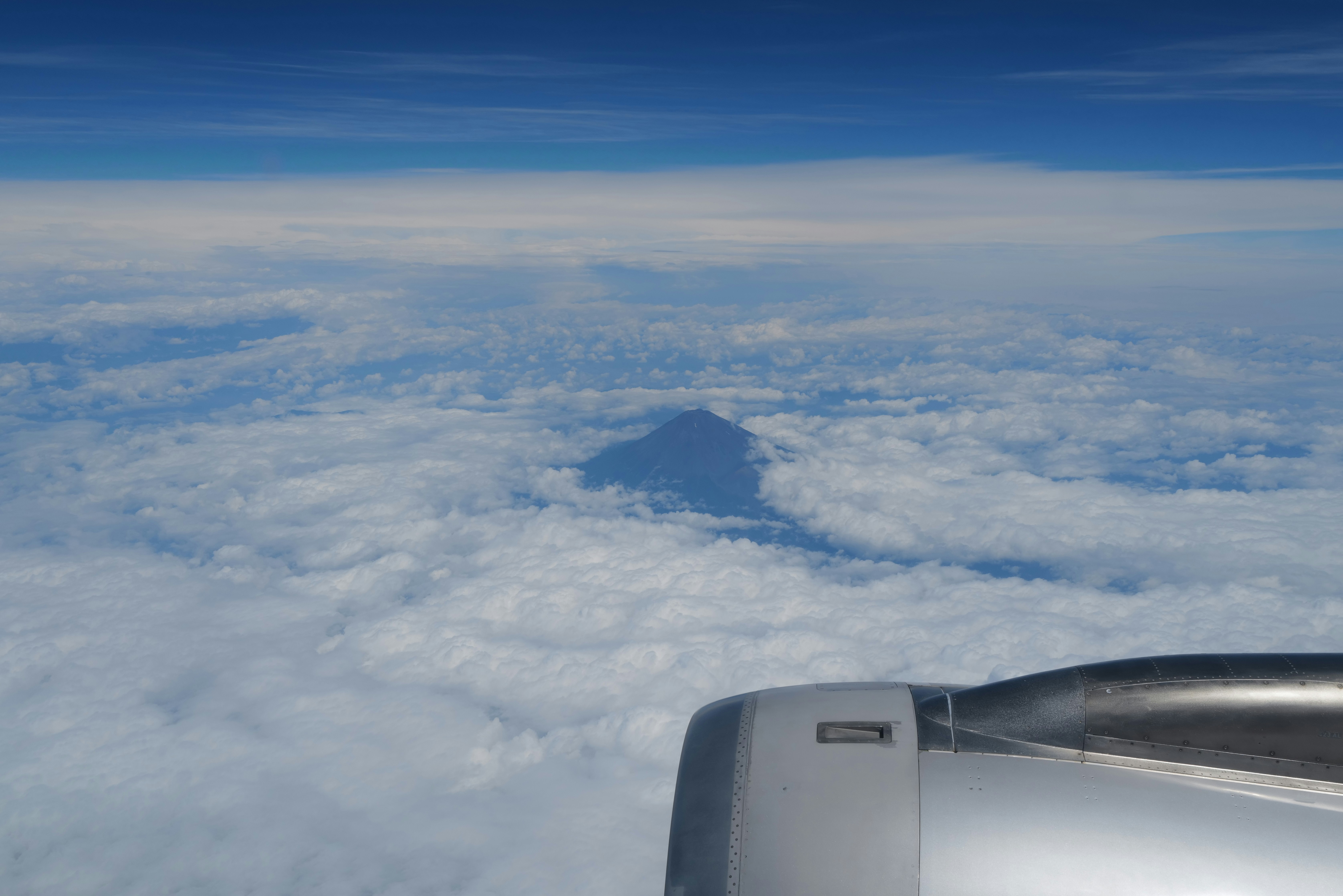 A mountain peak rising above a thick layer of clouds from an airplane window