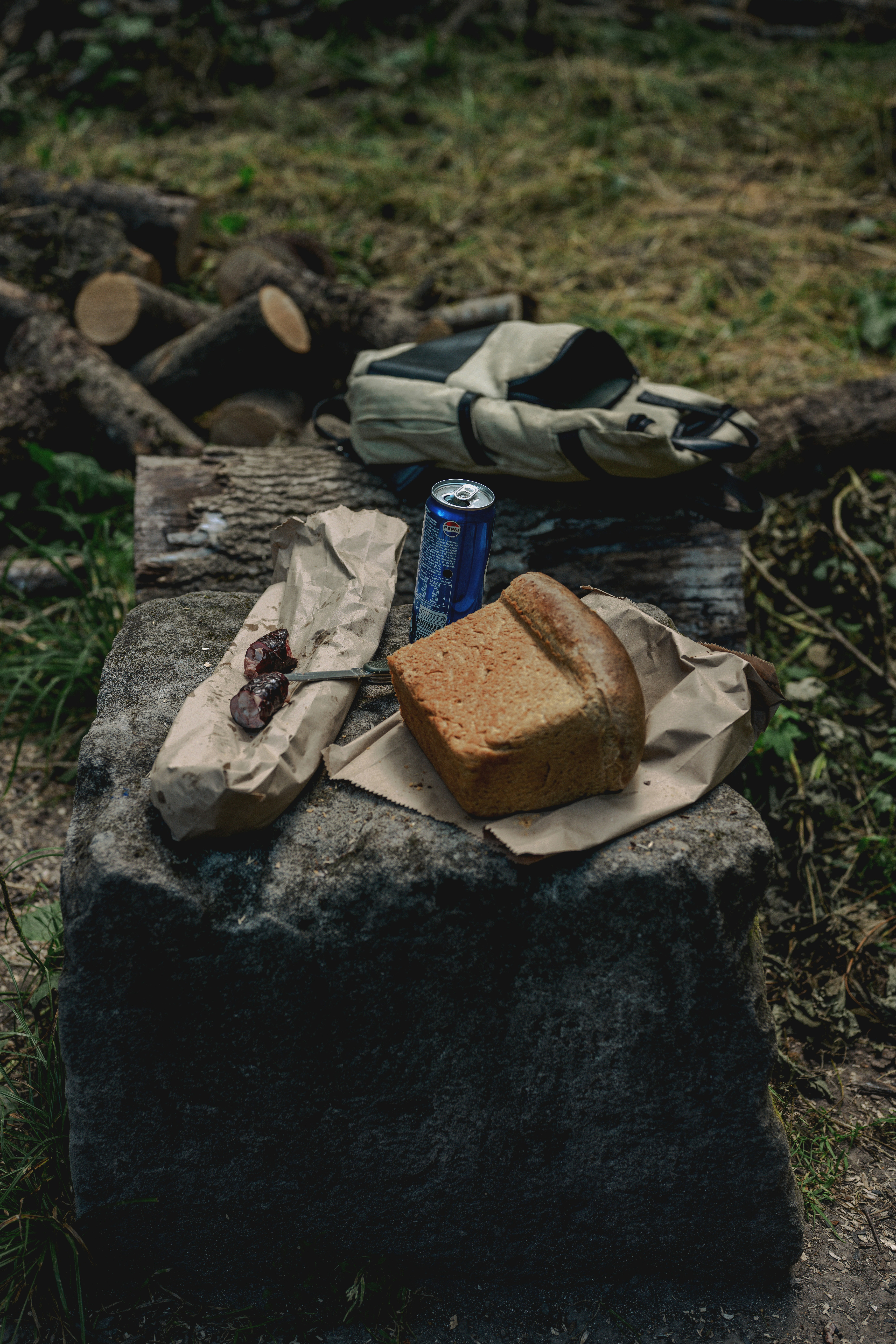 A loaf of bread, sausage, and a soda can on a stone block.