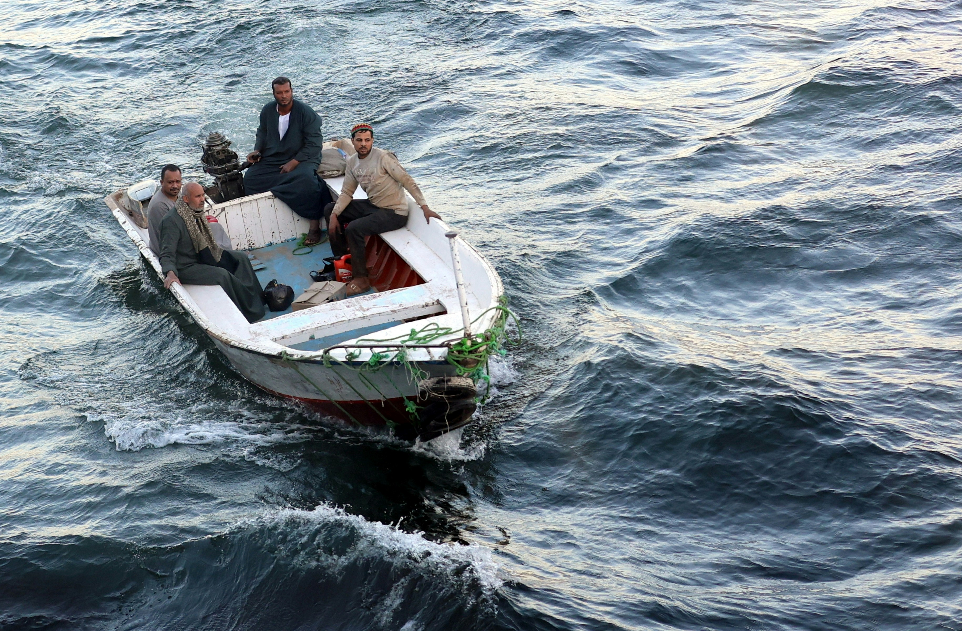 Four men in a small white motorboat on dark, choppy water.