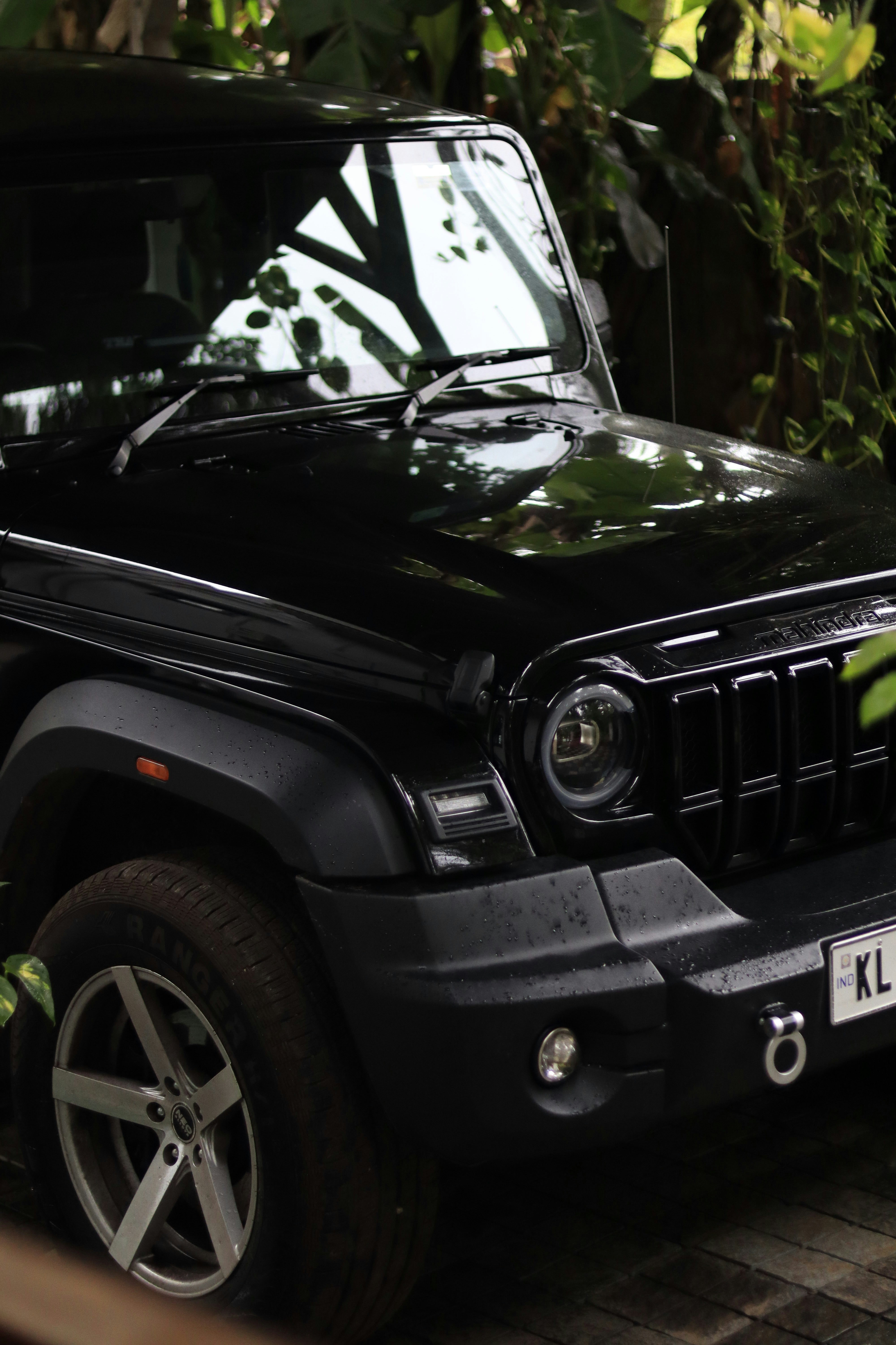 Un SUV noir Mahindra Thar garé dans un jardin luxuriant.