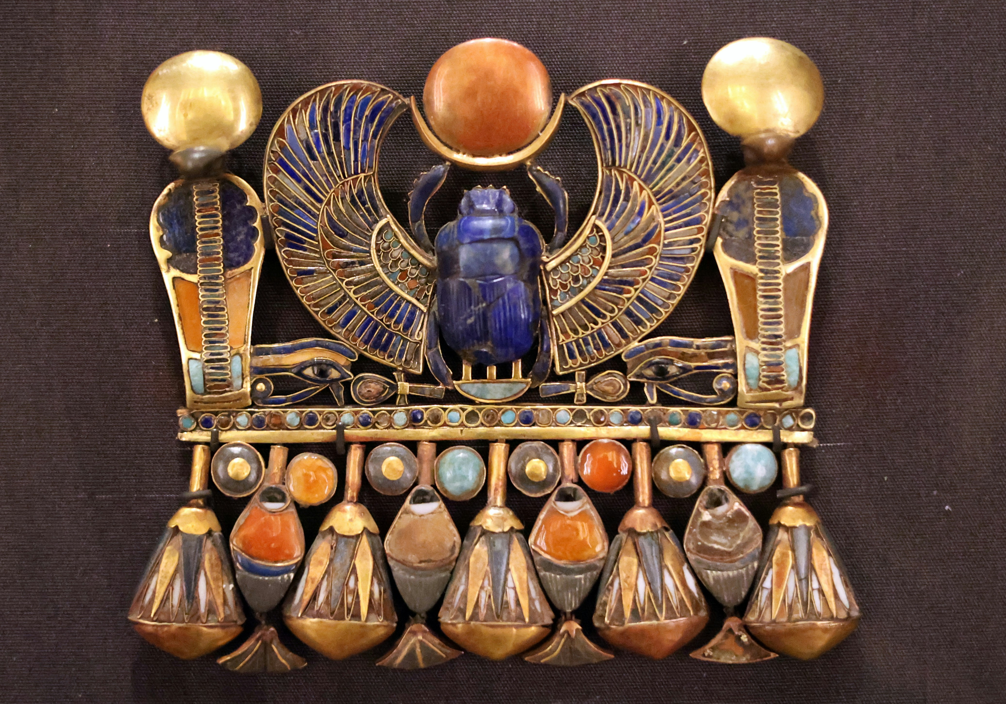 An ancient Egyptian gold pectoral featuring a winged scarab beetle and hanging lotus pendants.