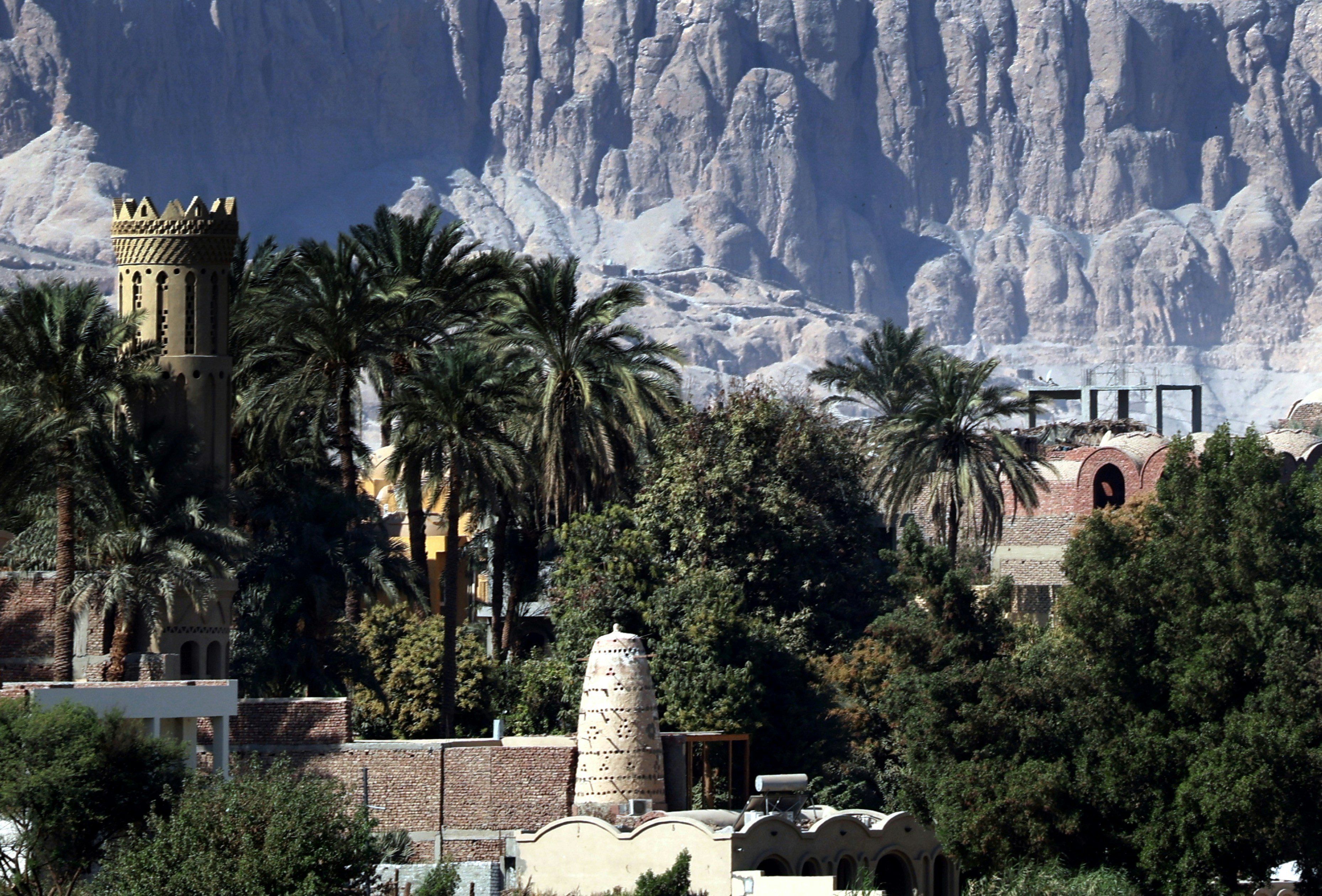 A tall tower and palm trees before a rugged mountain range in Luxor, Egypt.