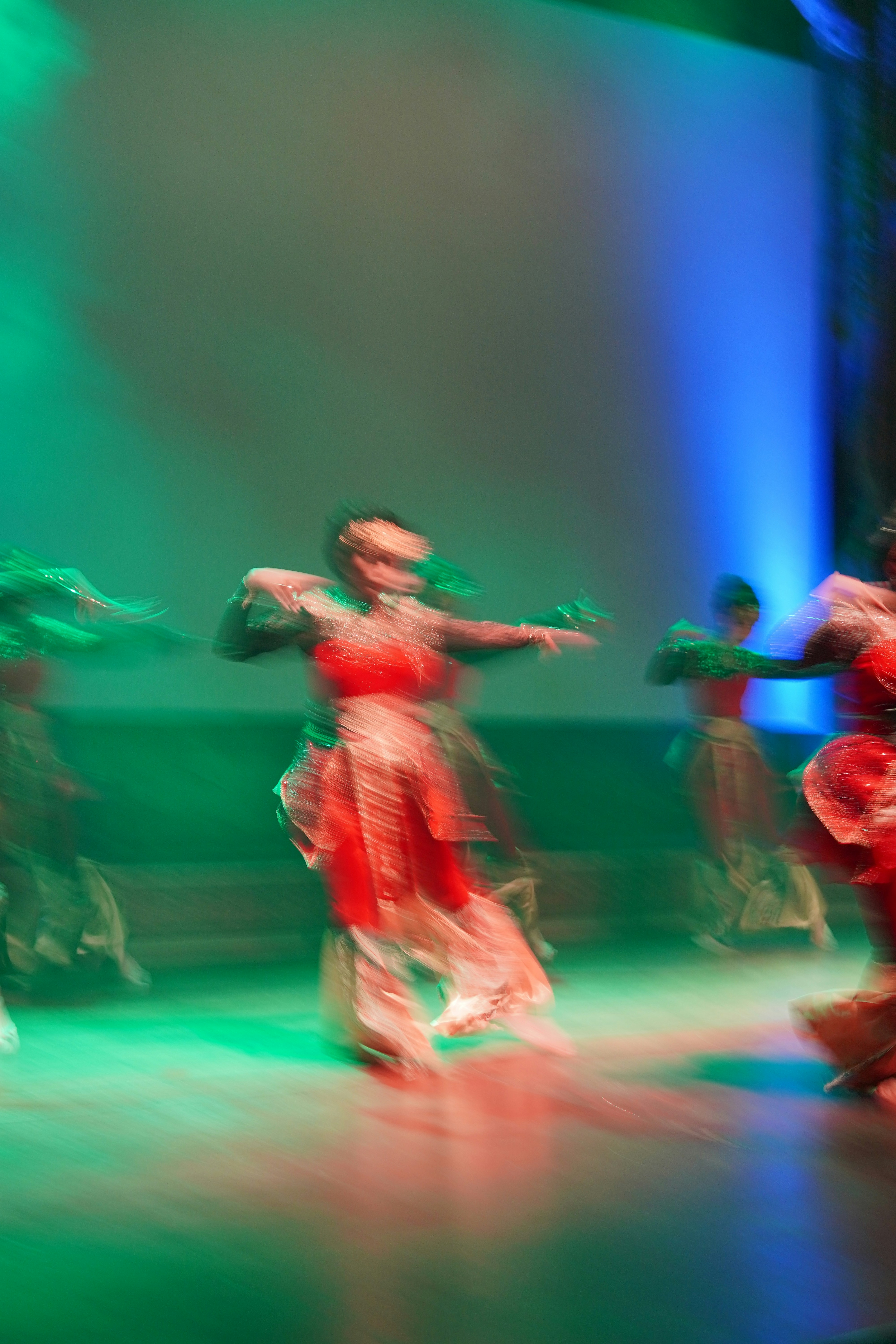 Dancers in red and gold costumes performing on a stage with green lighting