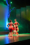 Two dancers in traditional red and gold costumes performing on a stage