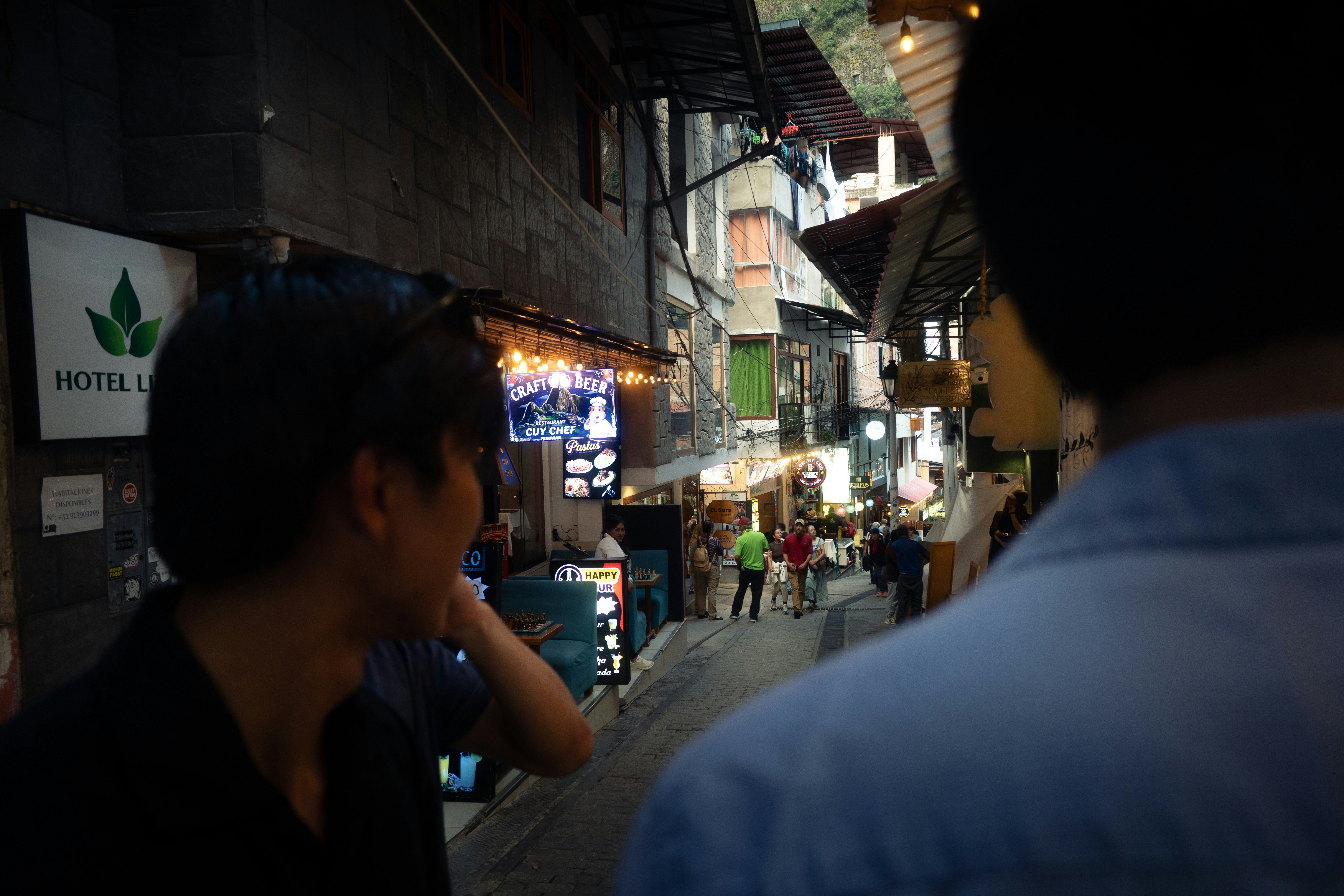 People walking along a narrow street lined with restaurants and glowing signs at night