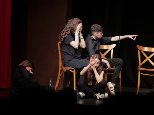 Three people in black clothing on a stage, one pointing to the side.