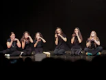 Six people in black clothing sitting on a stage, performing sign language