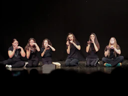 Six people in black clothing sitting on a stage, performing sign language