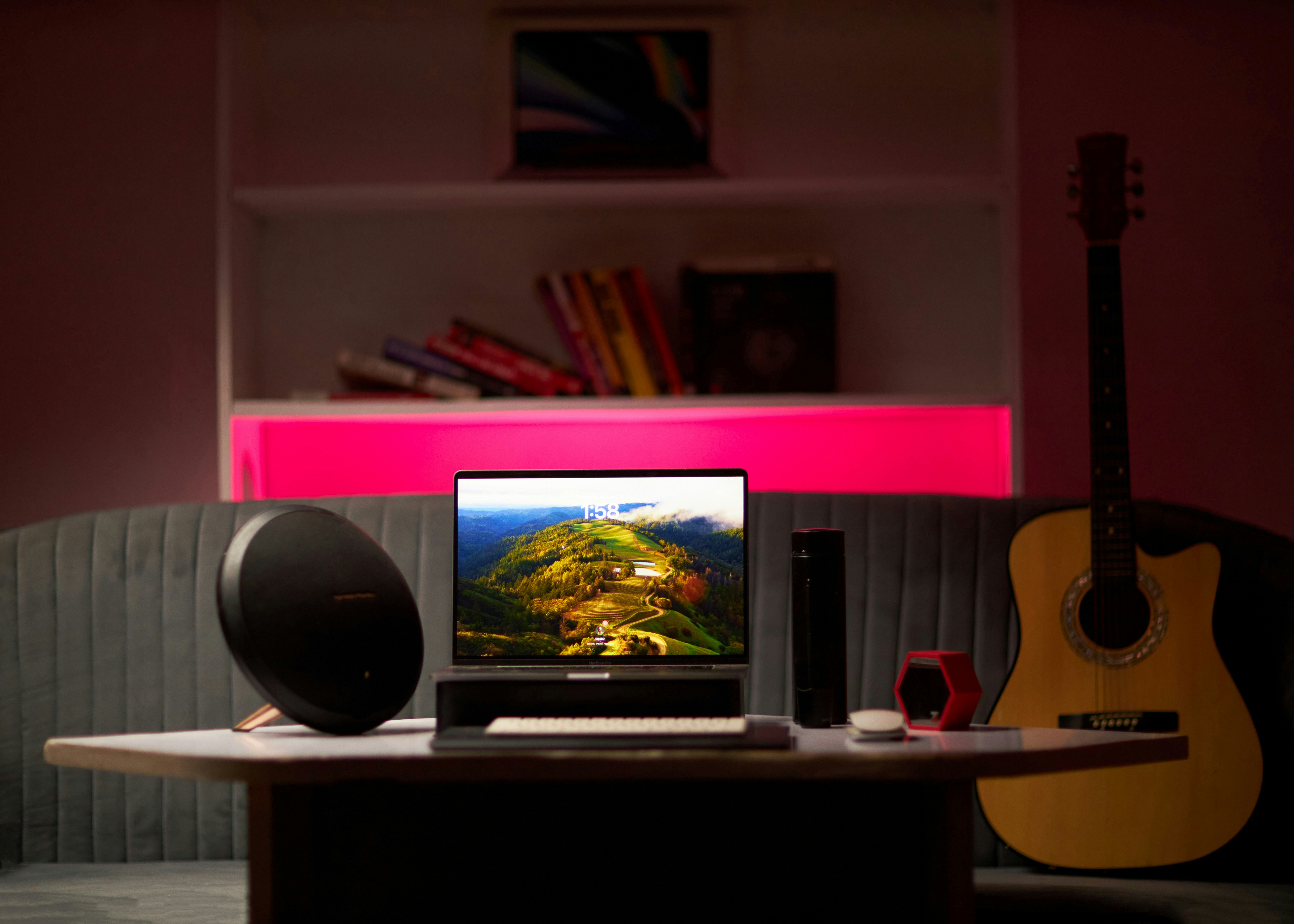 Un portátil, un altavoz y una guitarra acústica sobre una mesa en una habitación.