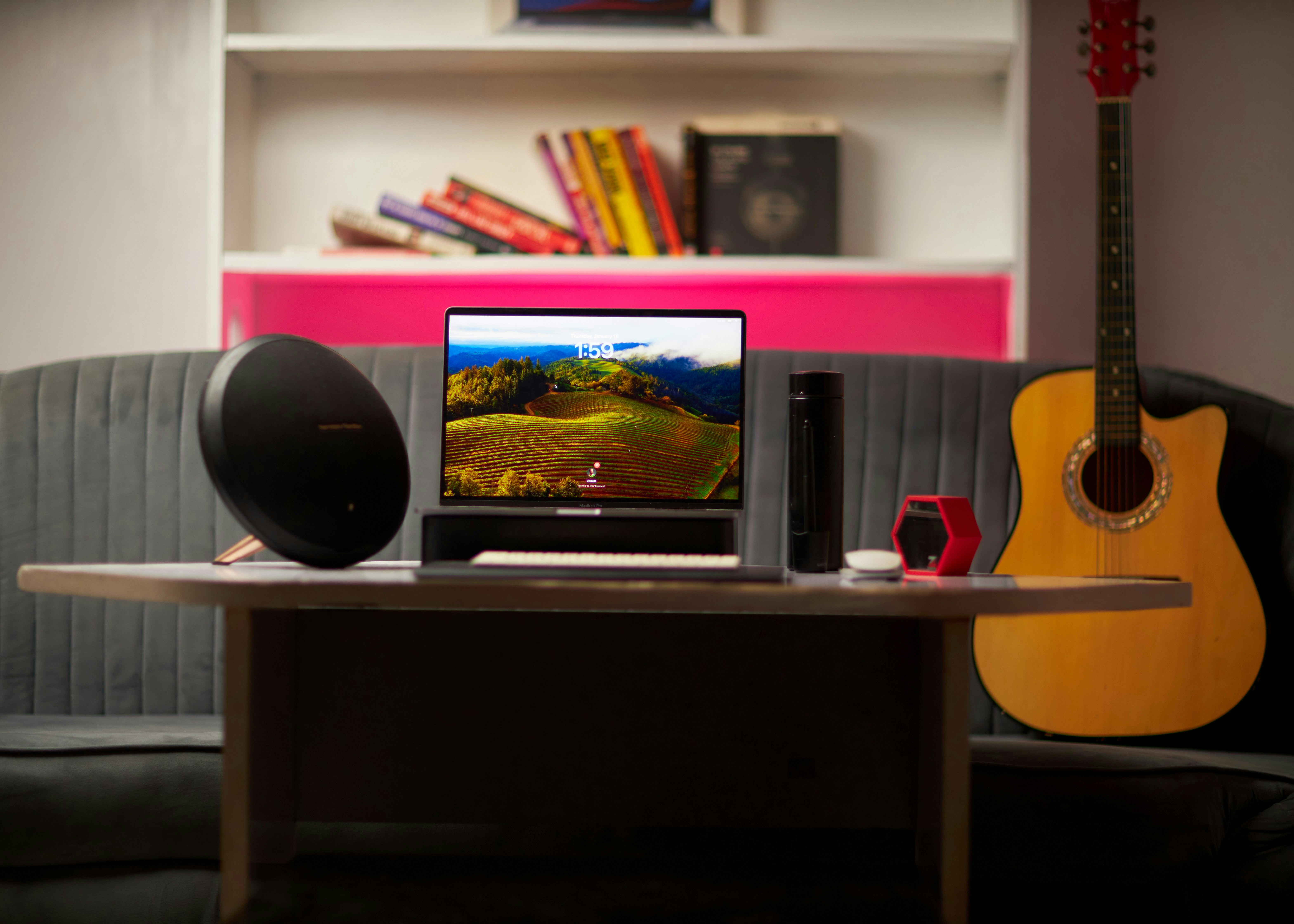 Un portátil, altavoz y guitarra acústica sobre un escritorio en una oficina en casa.