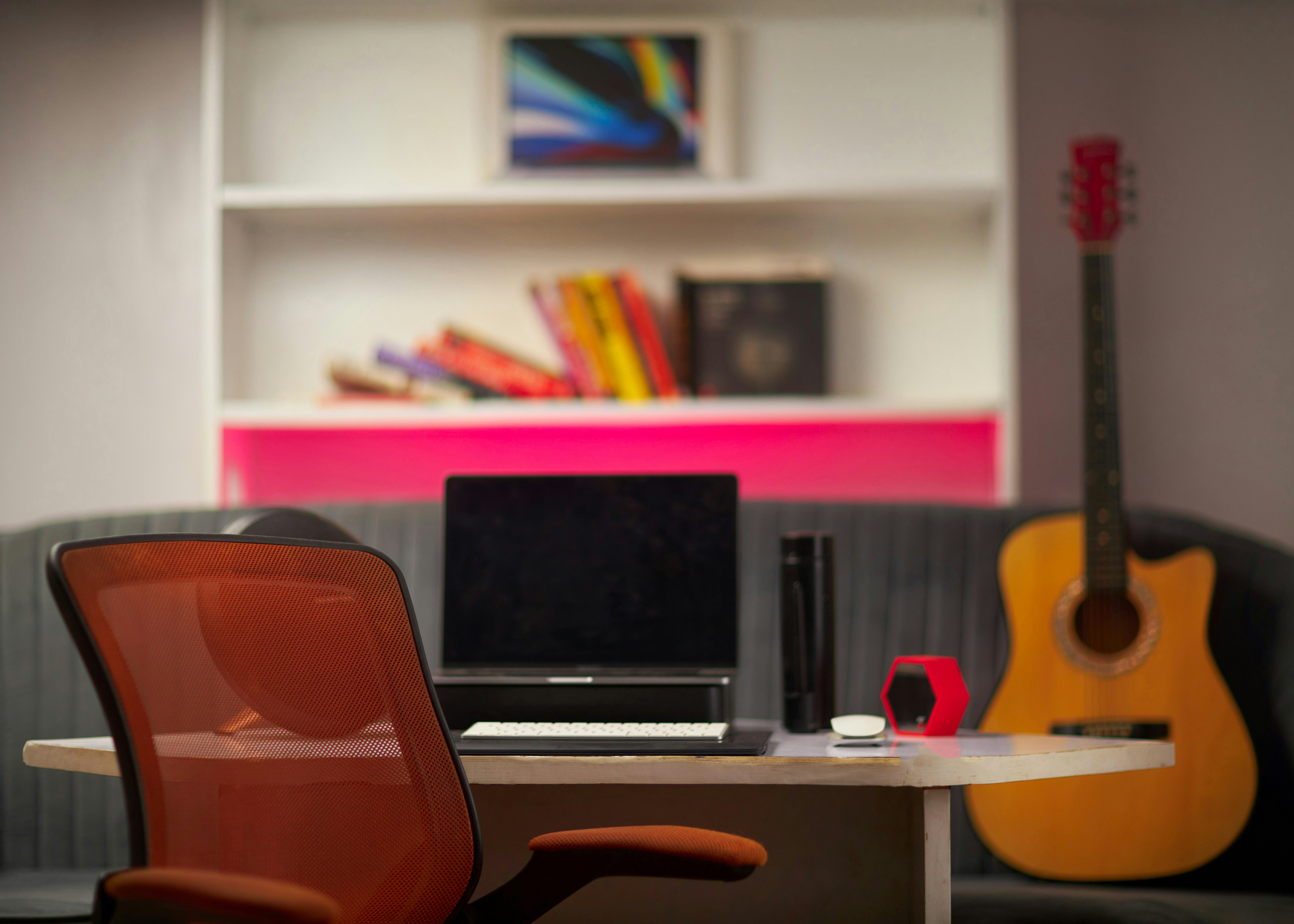Una silla de oficina de malla naranja en un escritorio con un portátil y una guitarra acústica.