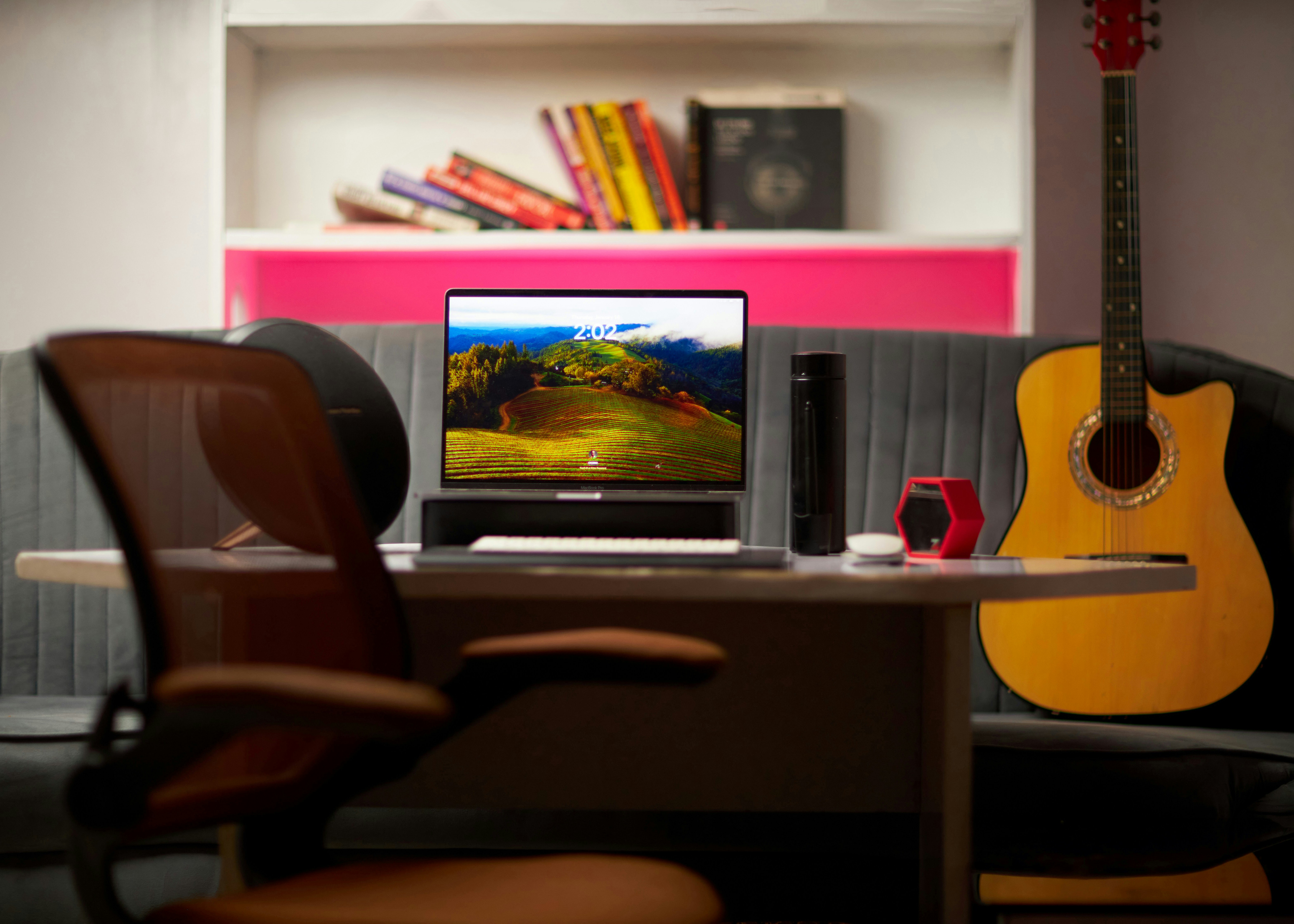 Un portátil sobre un escritorio con una guitarra y libros en una oficina en casa.