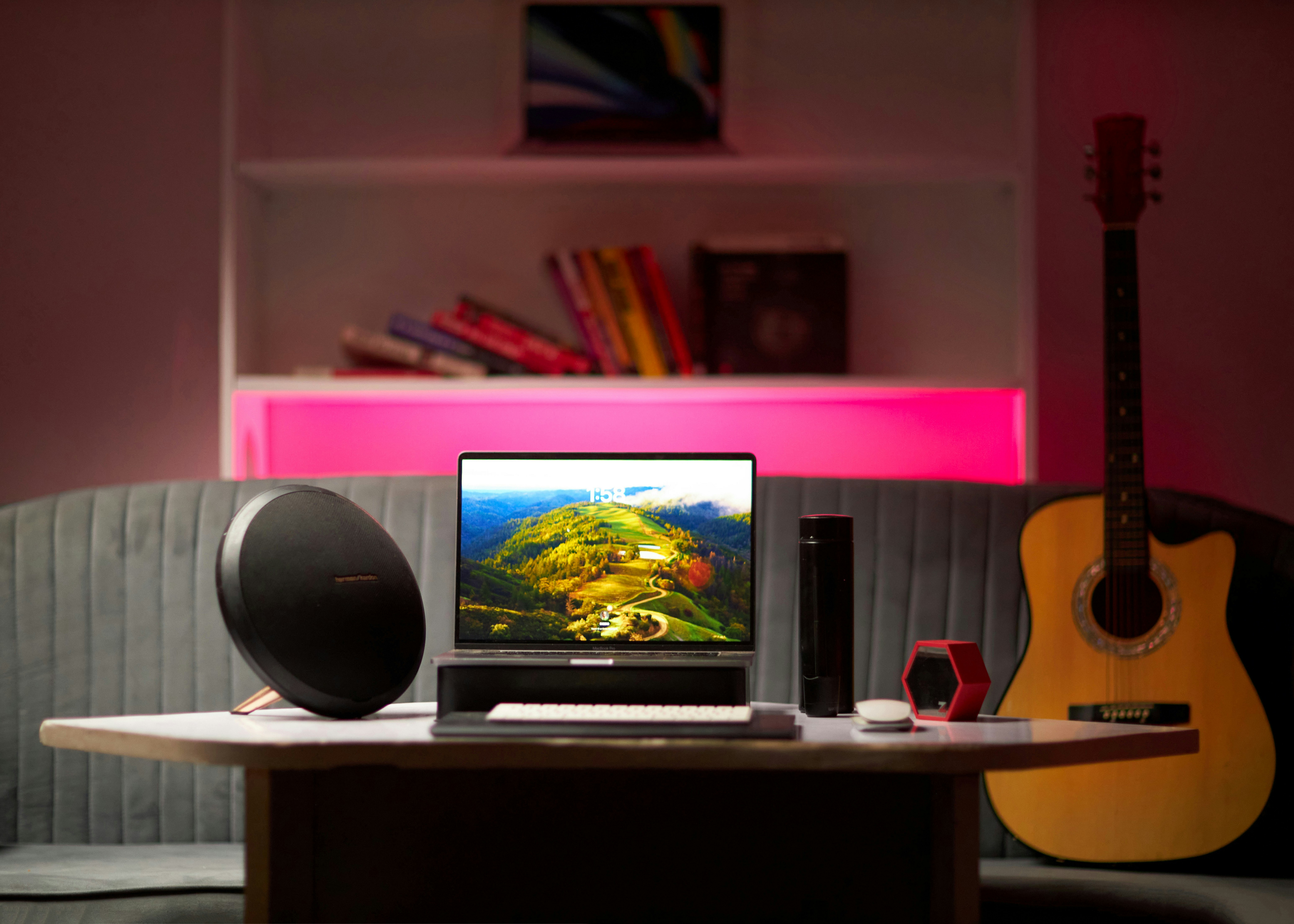 Un portátil, un altavoz redondo y una guitarra sobre un escritorio en una habitación.