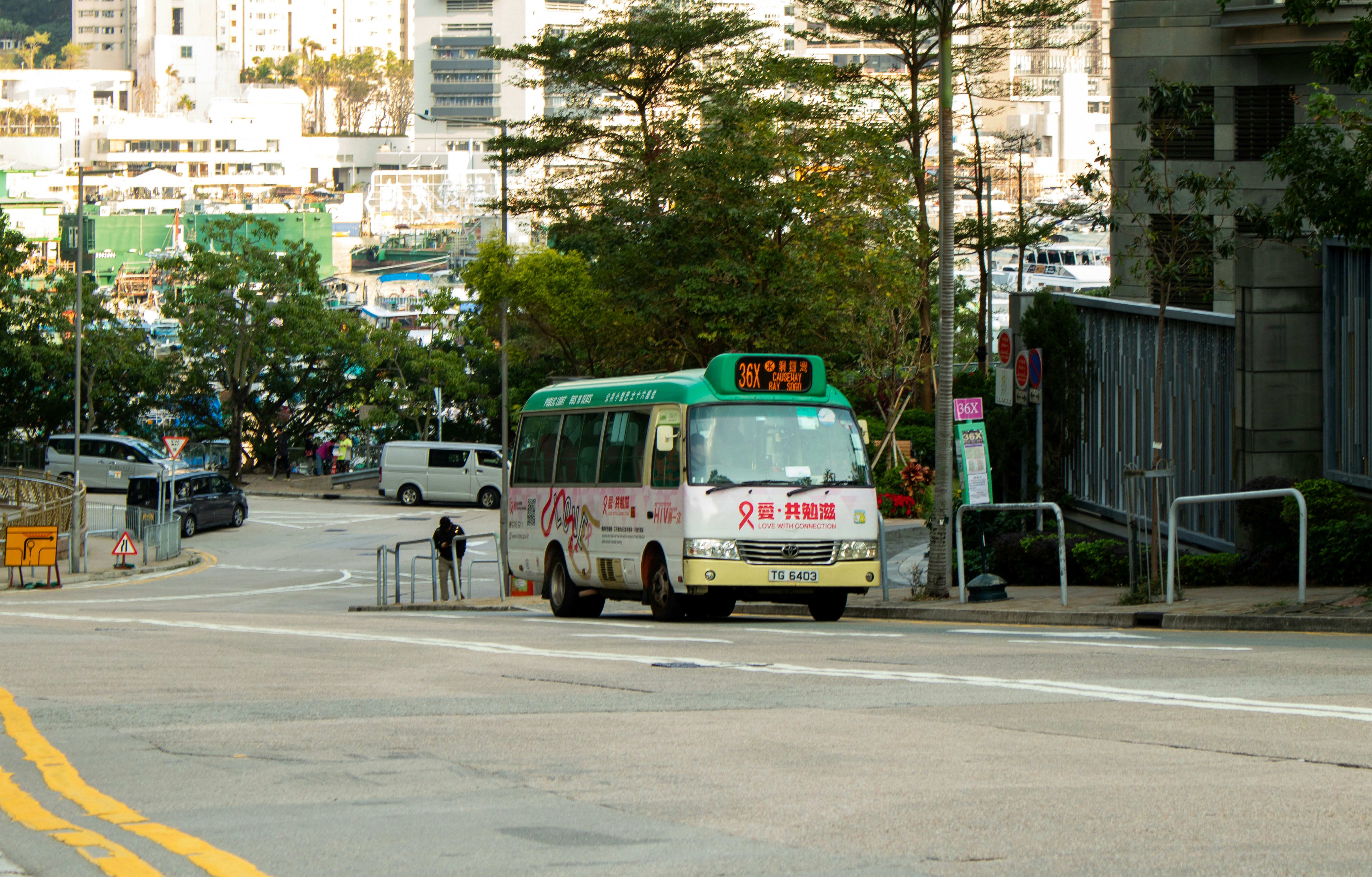 A green and white minibus on a city street near a harbor.