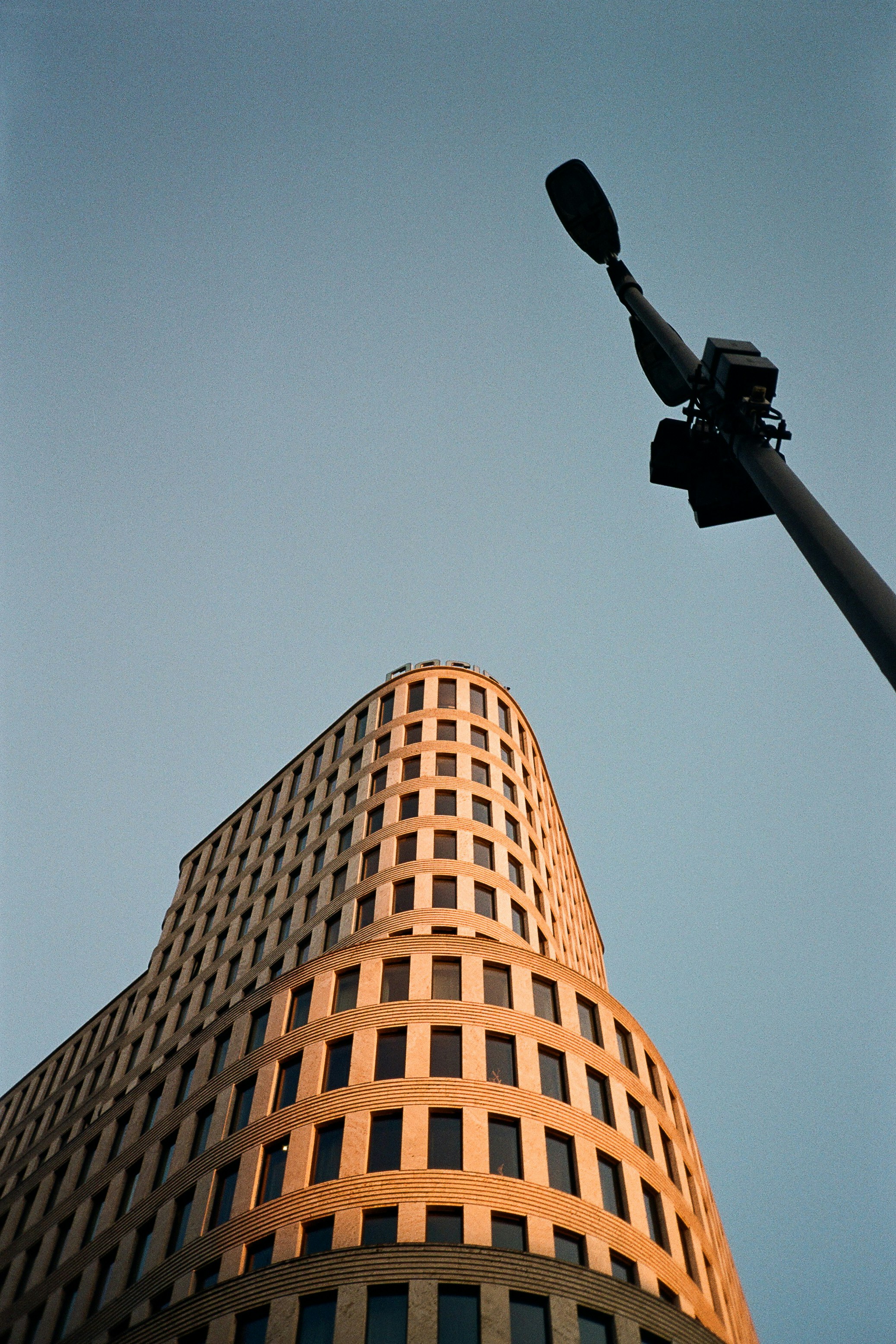A curved modern building in Berlin lit by warm light against a clear sky.
