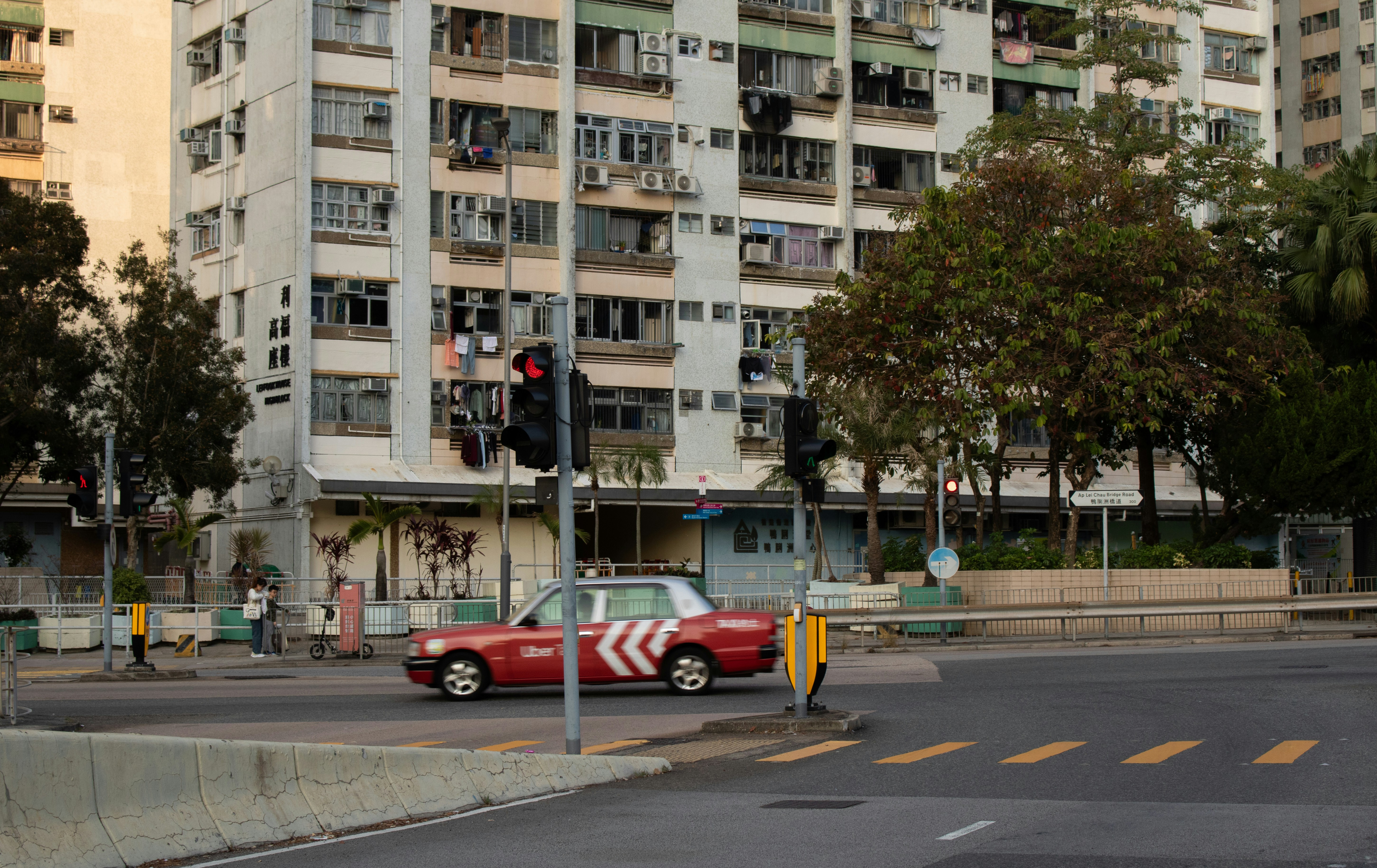 A red taxi driving past a tall residential building in Hong Kong