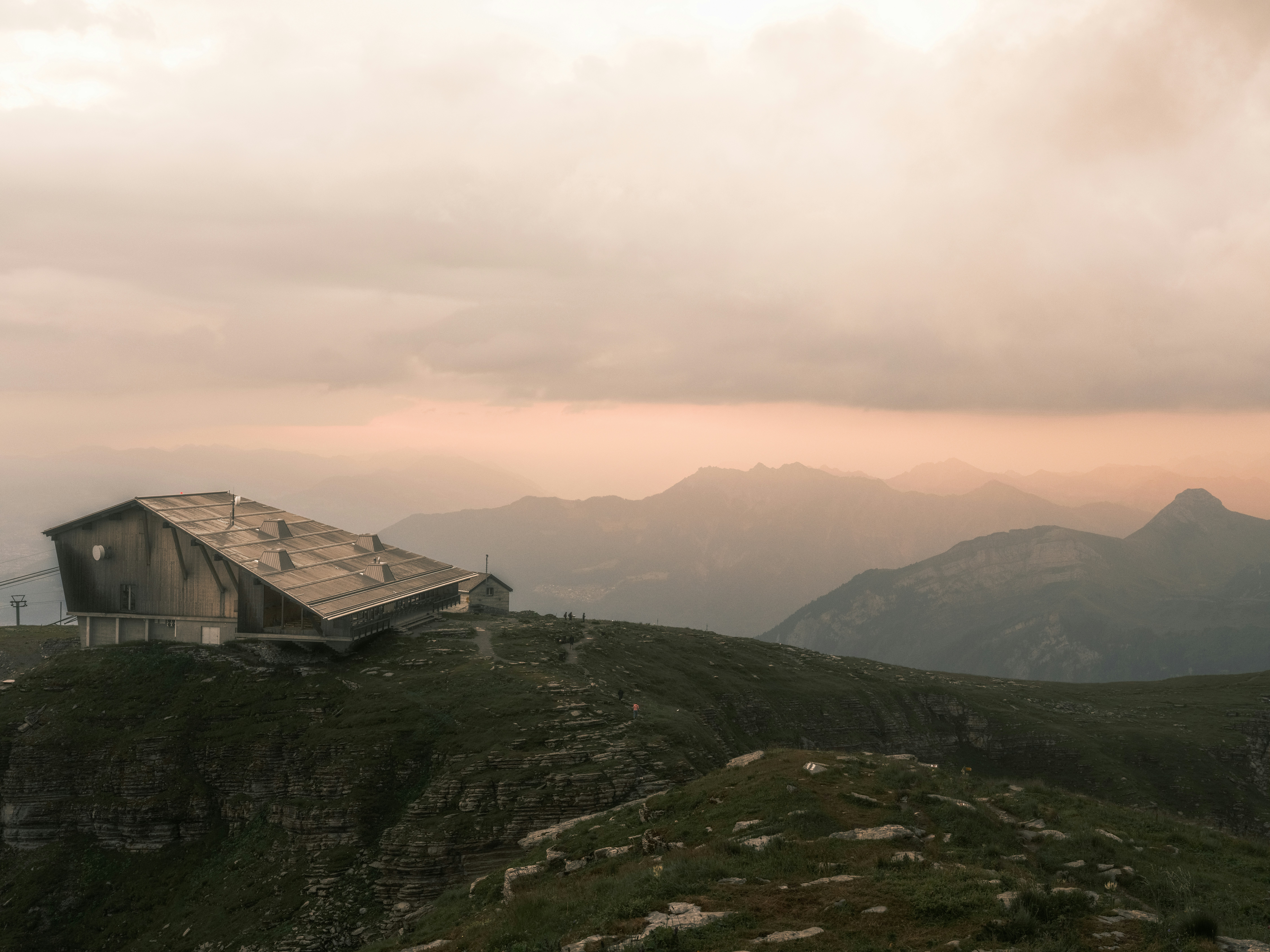 A wooden mountain lodge on a rocky ridge under a soft orange sky.