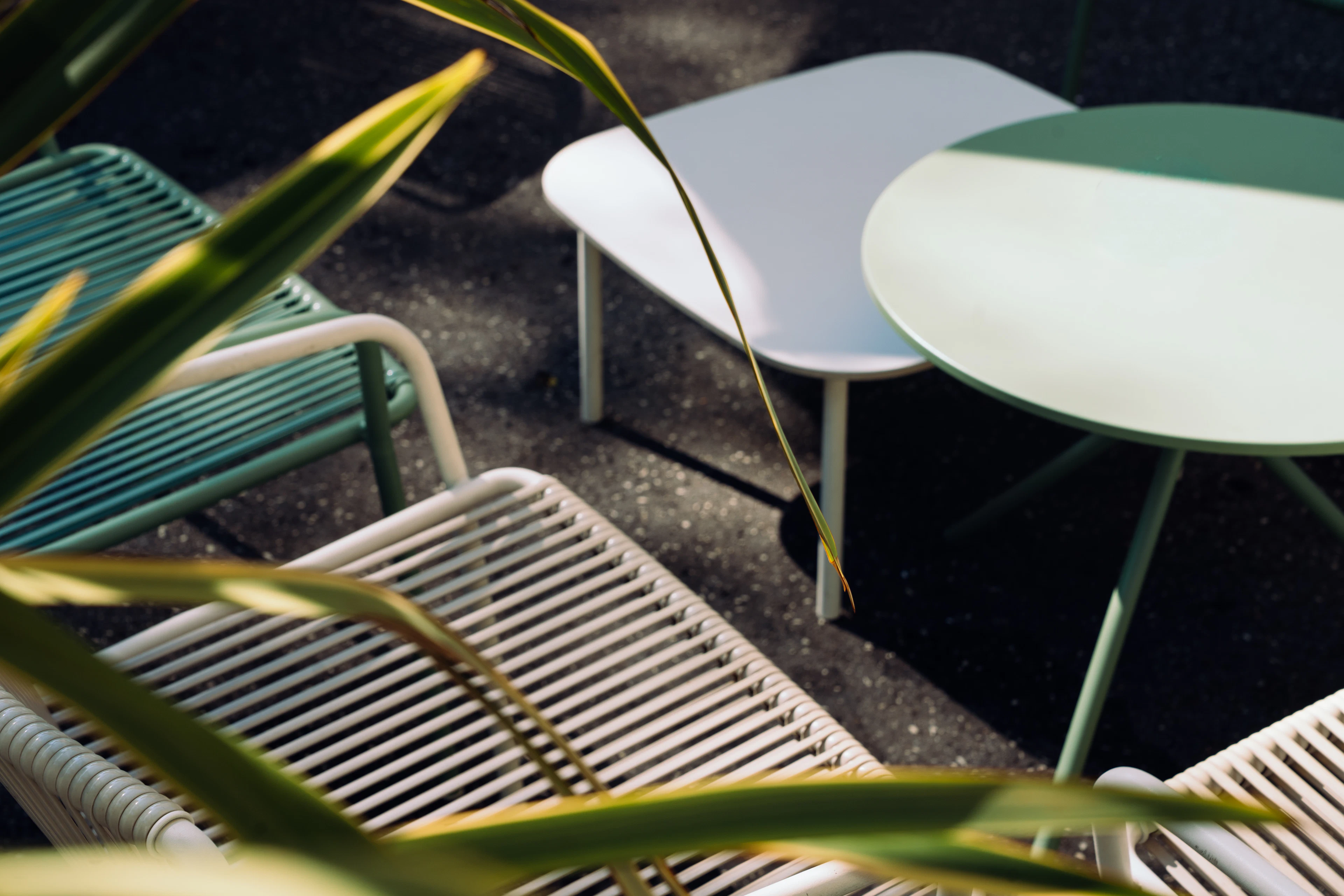 Modern outdoor chairs and tables on a dark patio framed by leaves