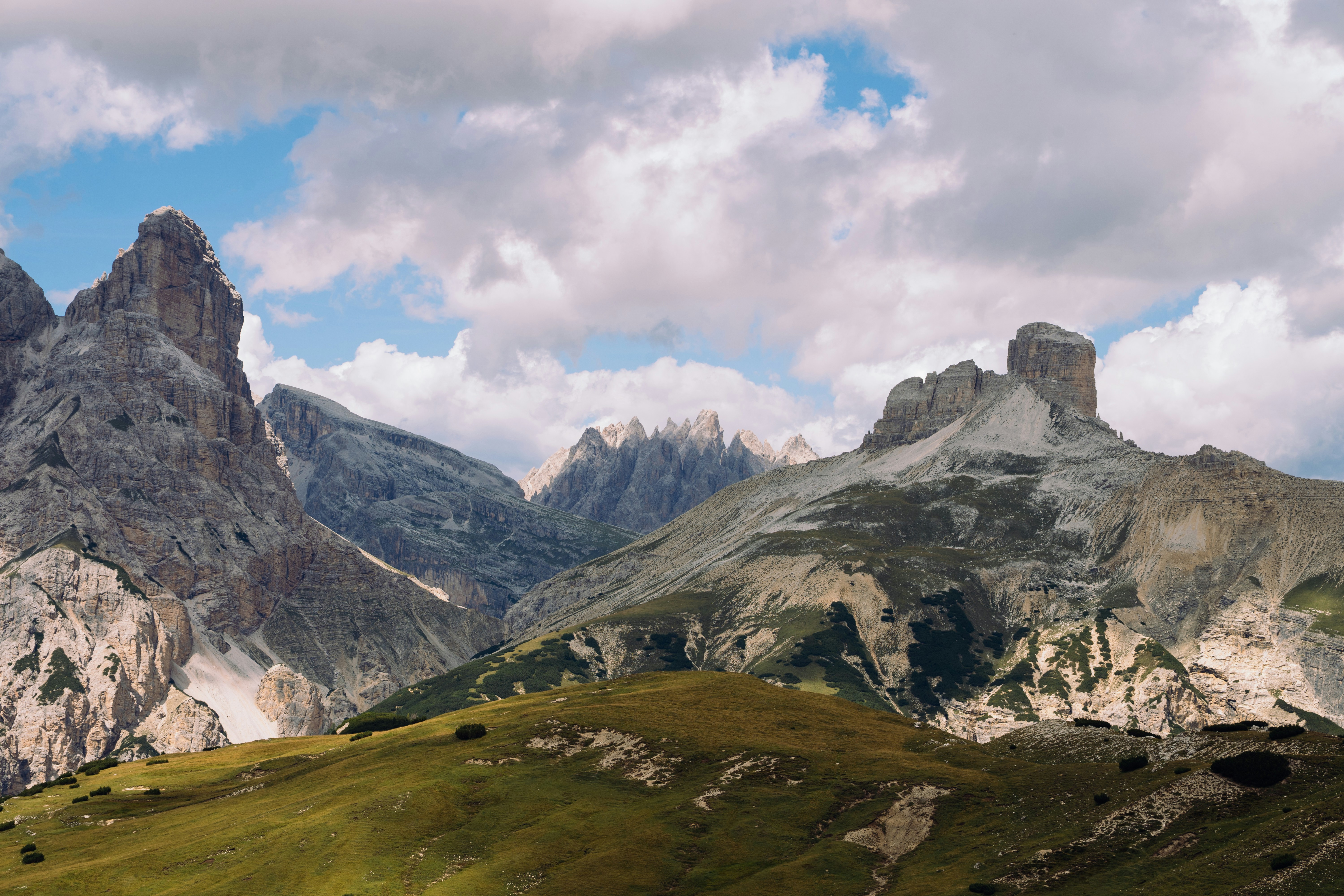 Cumbres de montañas rocosas que se elevan sobre una ladera verde cubierta de hierba bajo un cielo nublado