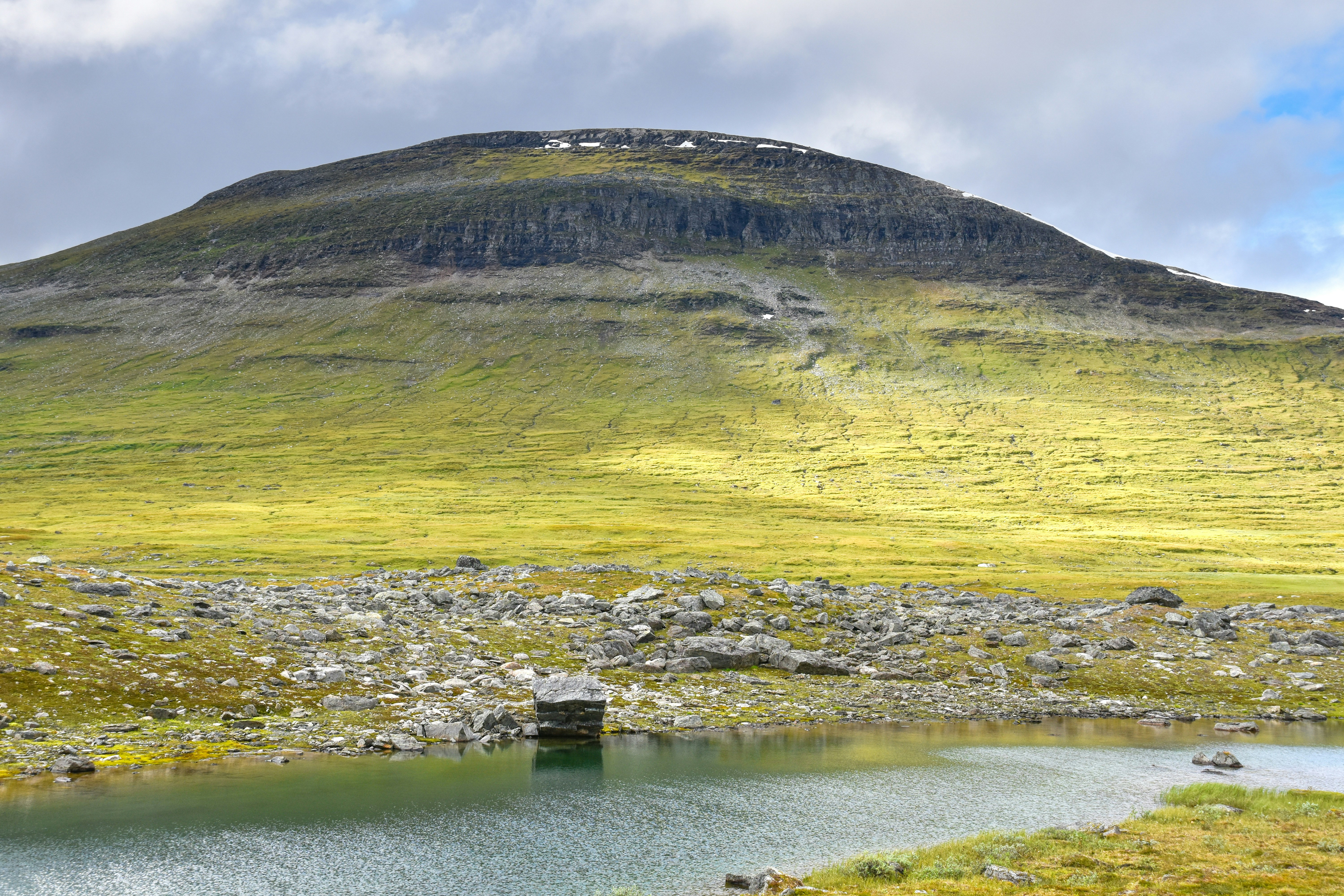 A green mountain slope above a rocky shoreline and a calm lake