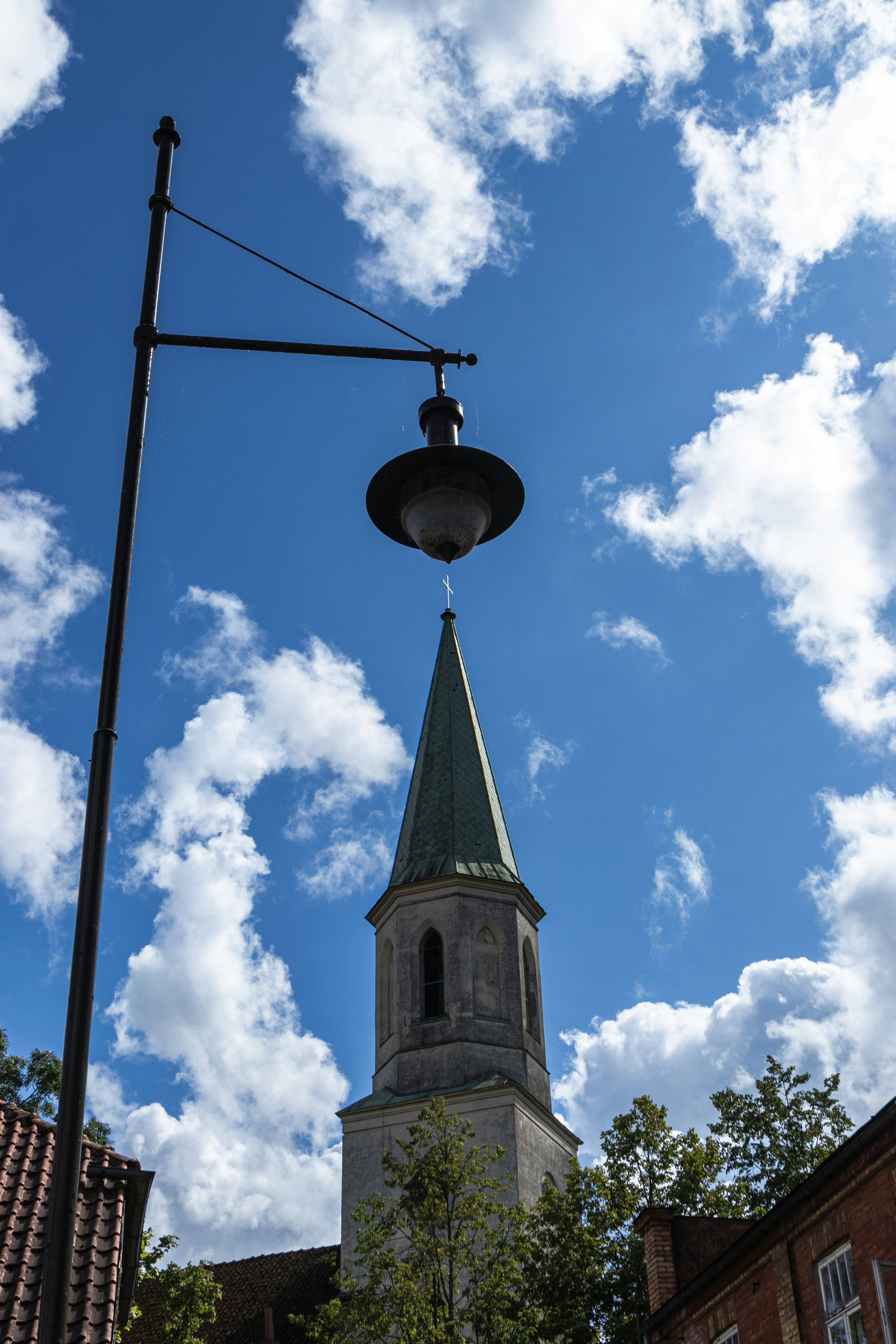 A black street lamp in front of a church steeple under a blue sky