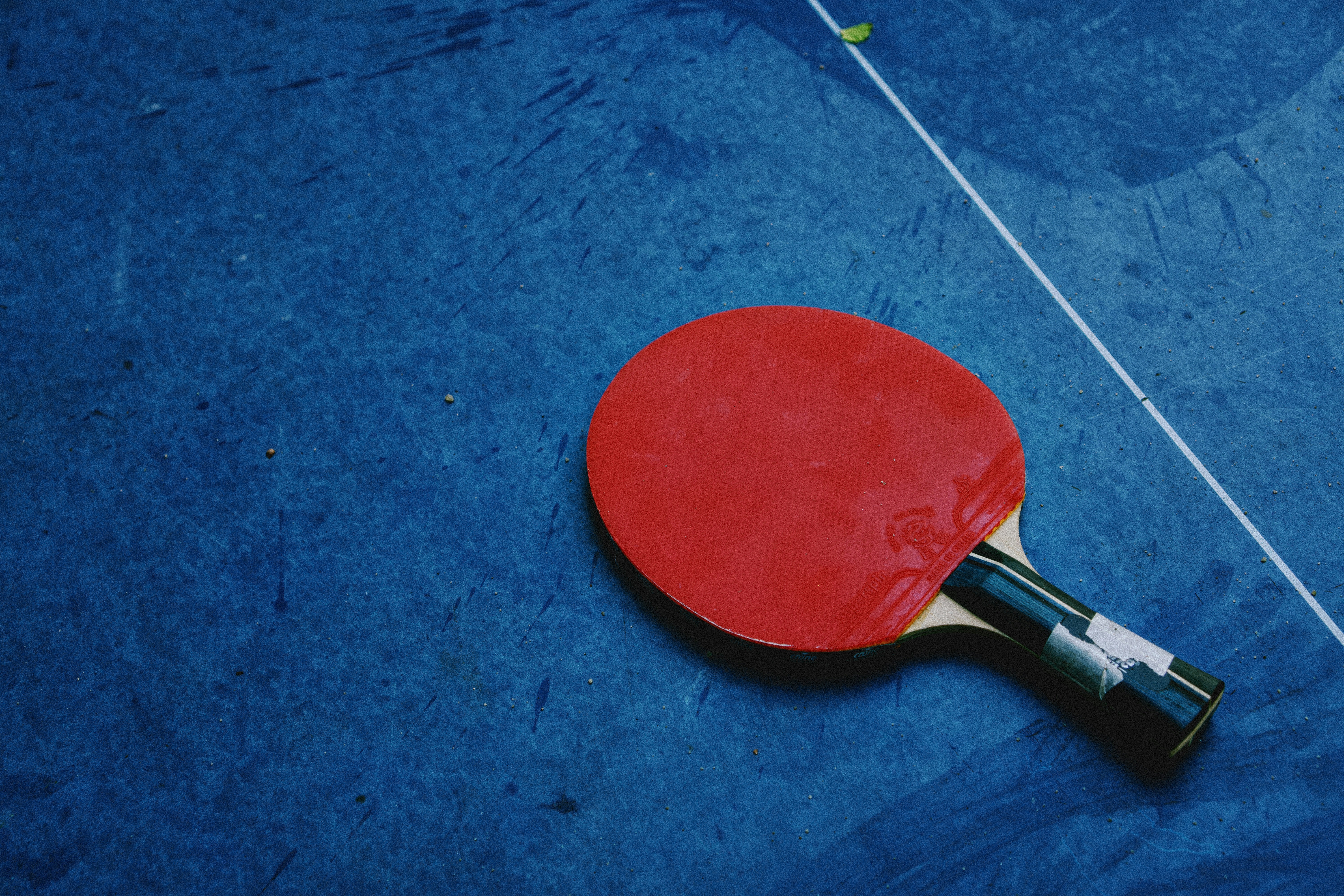 A red table tennis paddle resting on a blue table surface