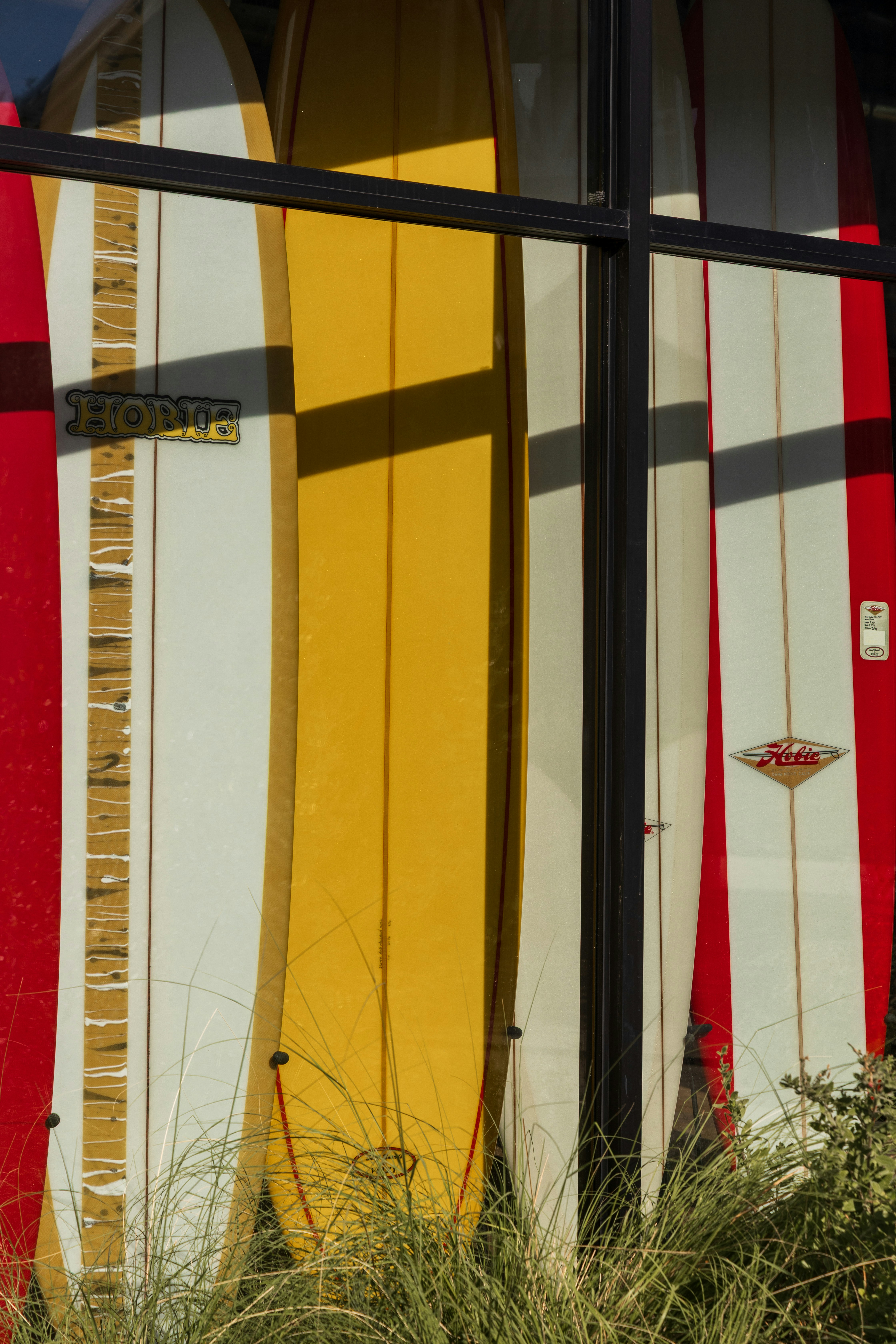 Three surfboards in red, yellow, and white standing behind a glass window.