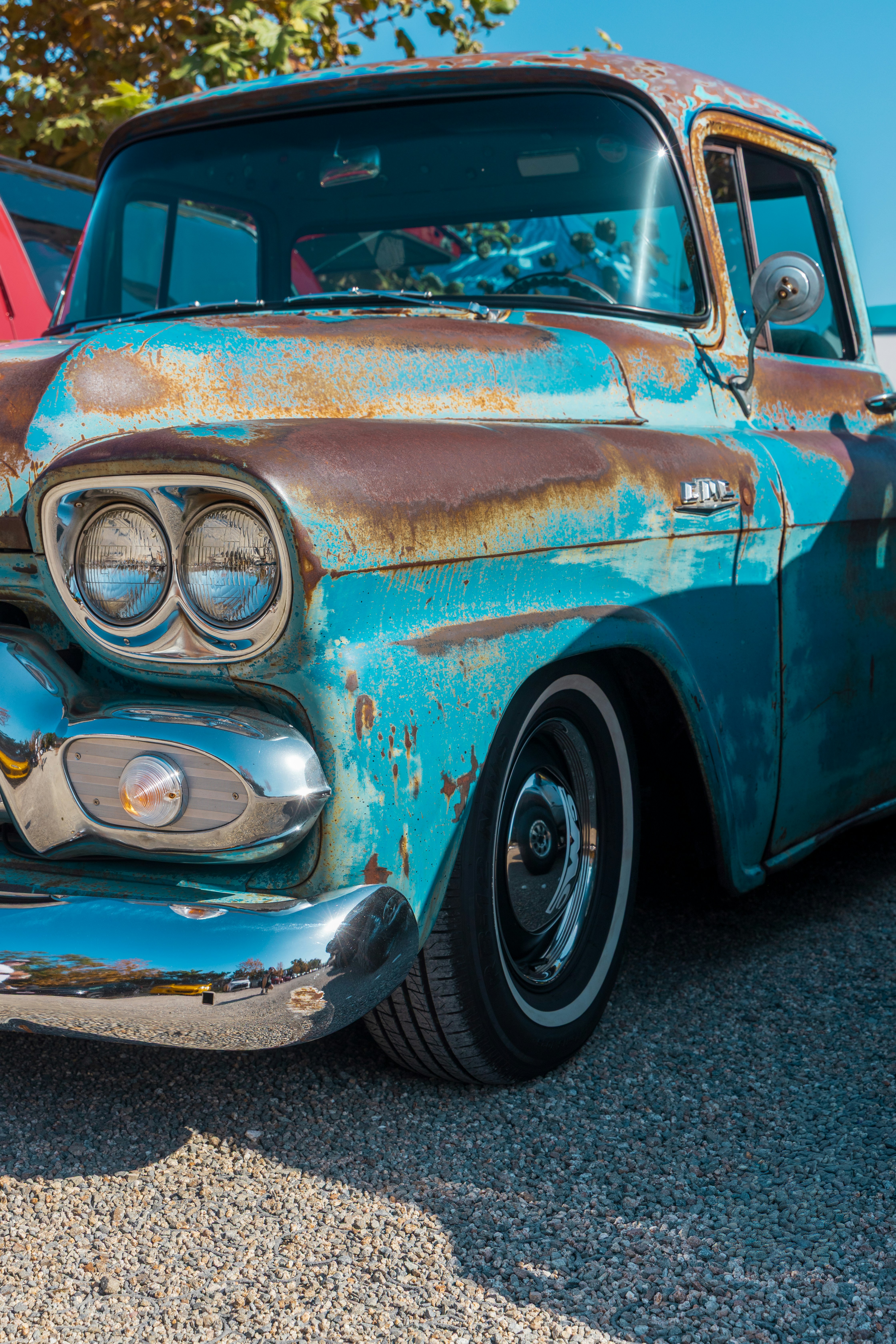 A vintage turquoise pickup truck with rust patches parked on a gravel lot.