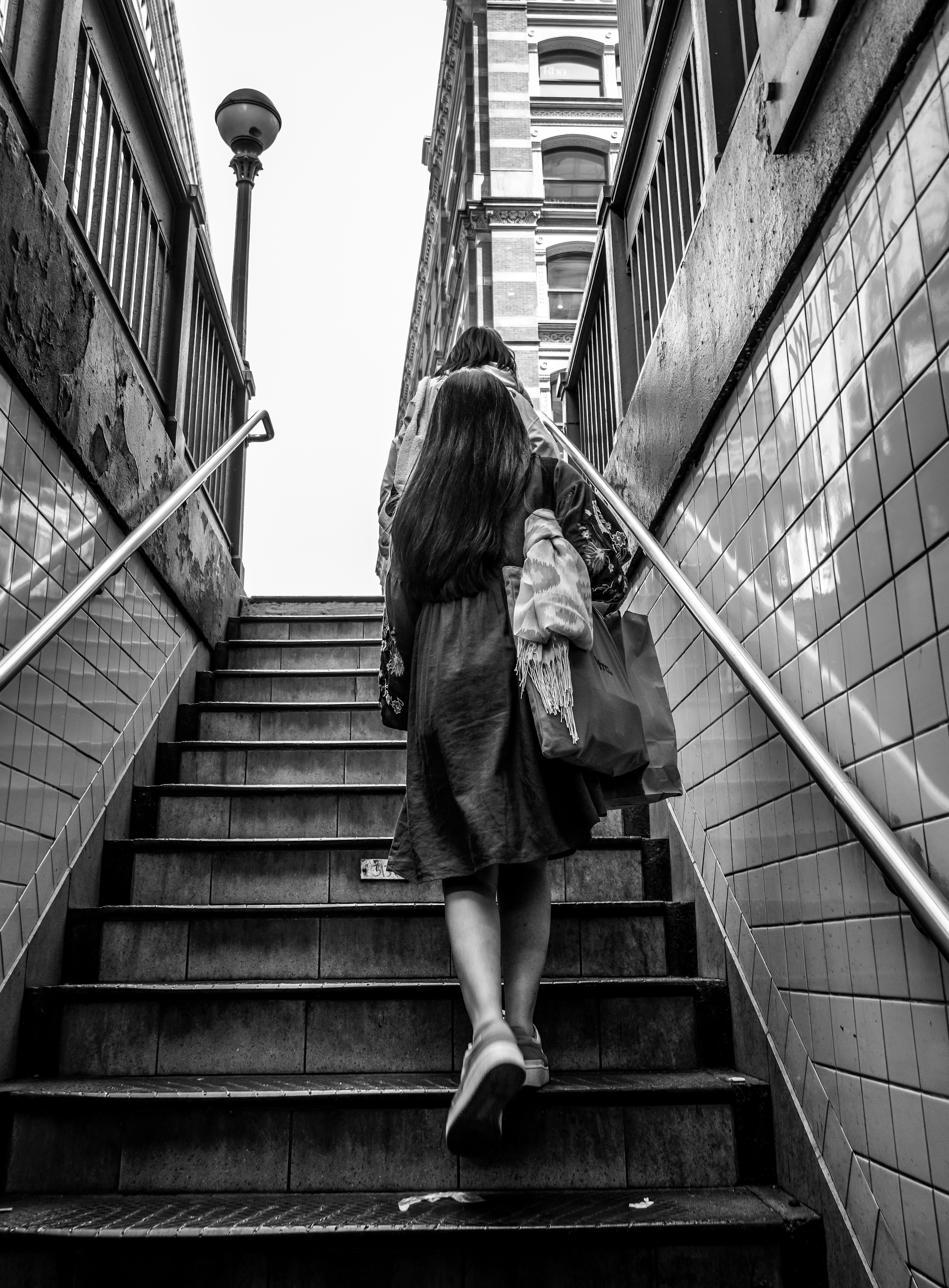 Two people walking up tiled subway stairs toward a city street in black and white