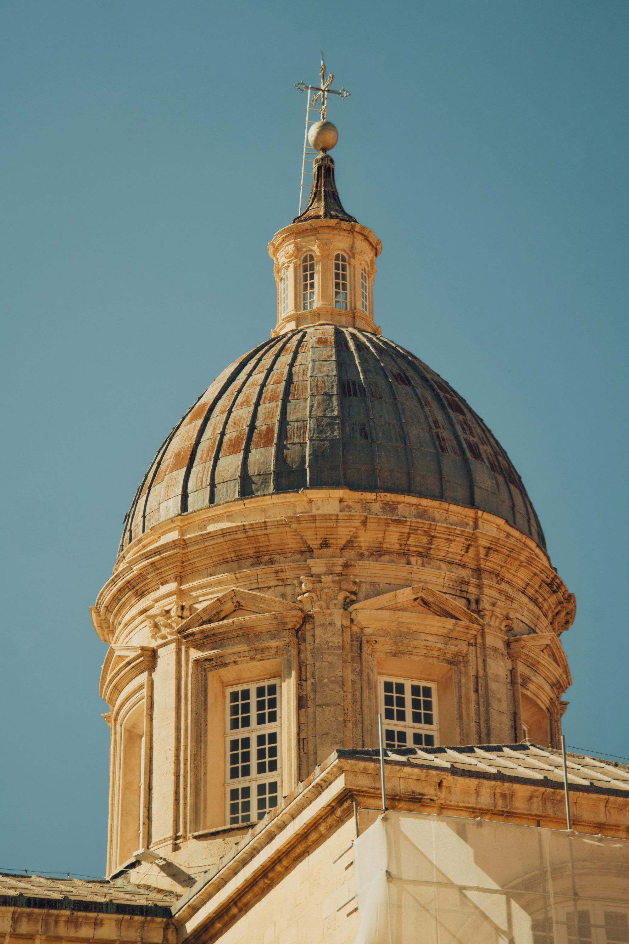 A weathered stone dome with a metal cross against a clear blue sky.