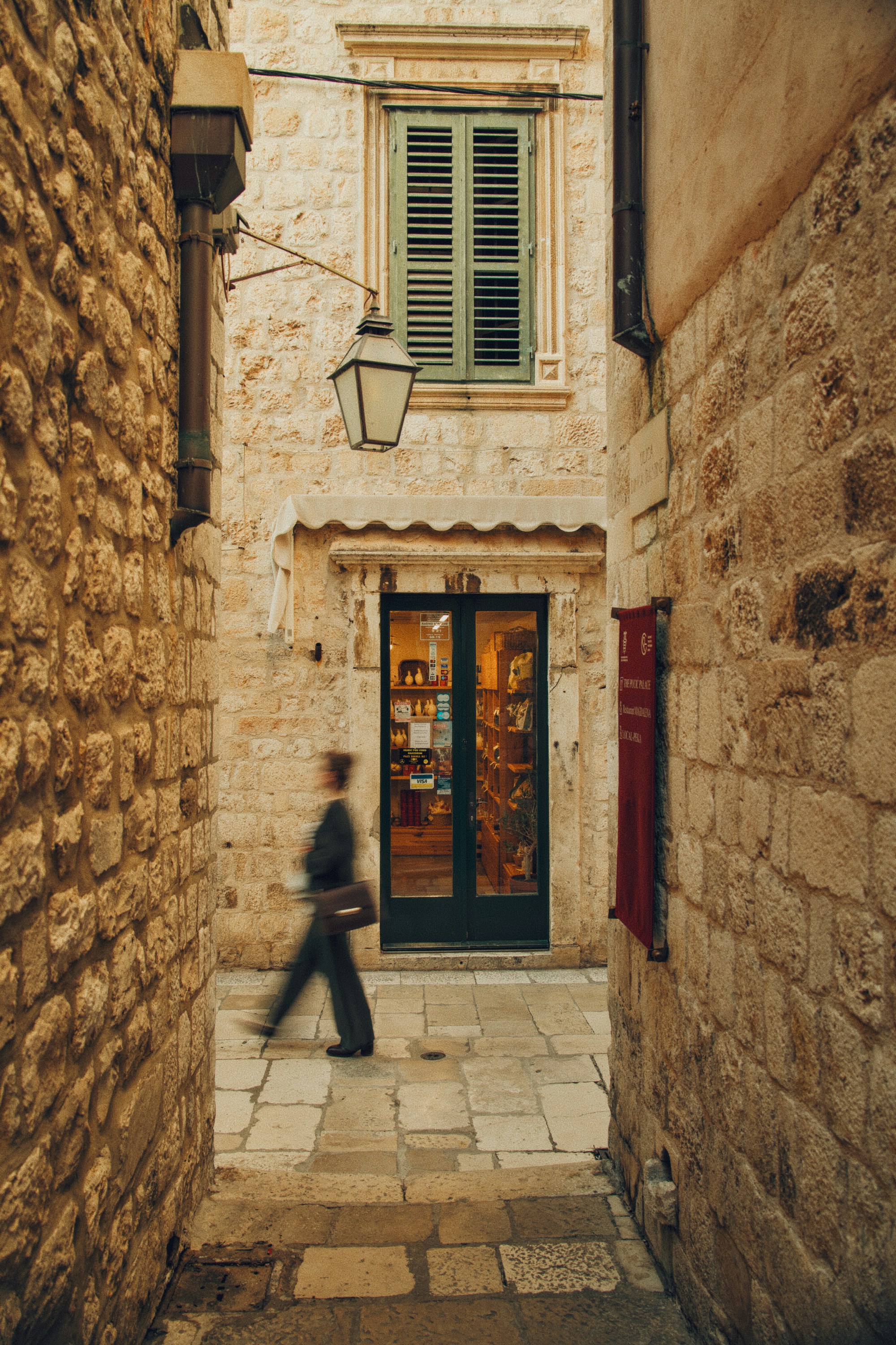 A person walking through a narrow stone alleyway in Dubrovnik, Croatia.