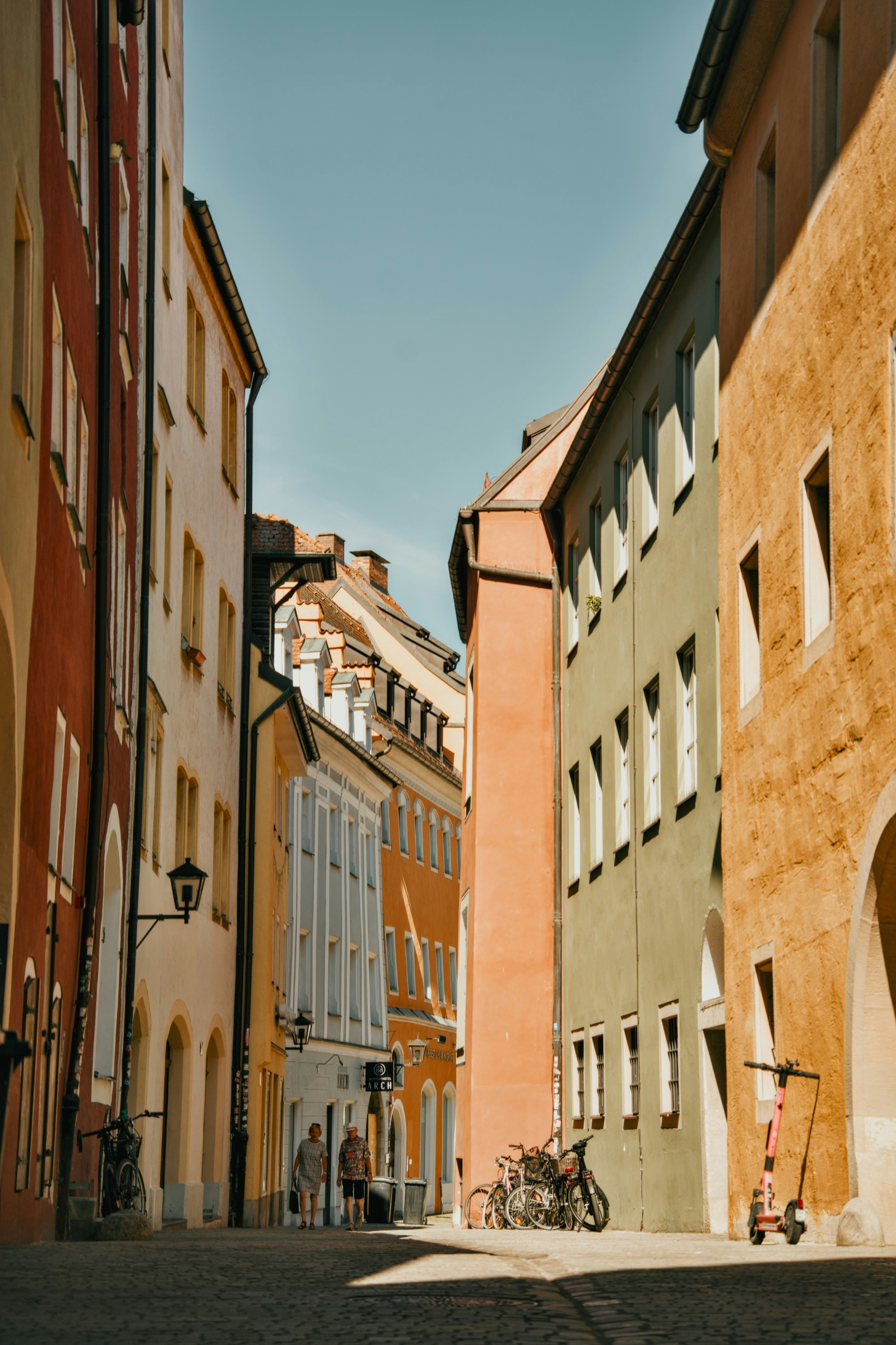 Two people walking down a narrow street lined with colorful historic buildings.