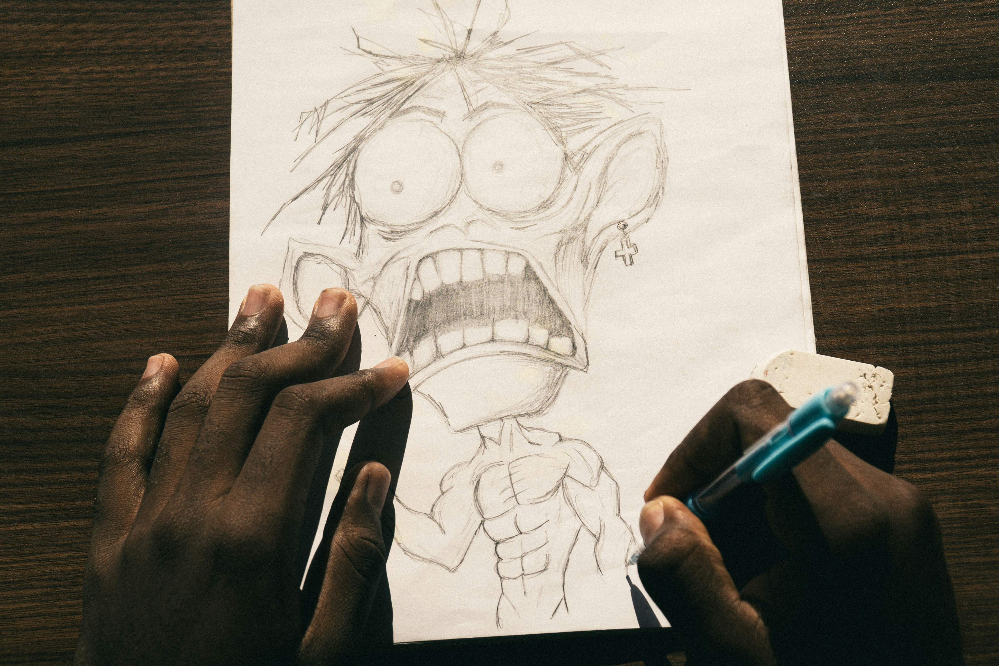 A person drawing a cartoon character with a large head on white paper.