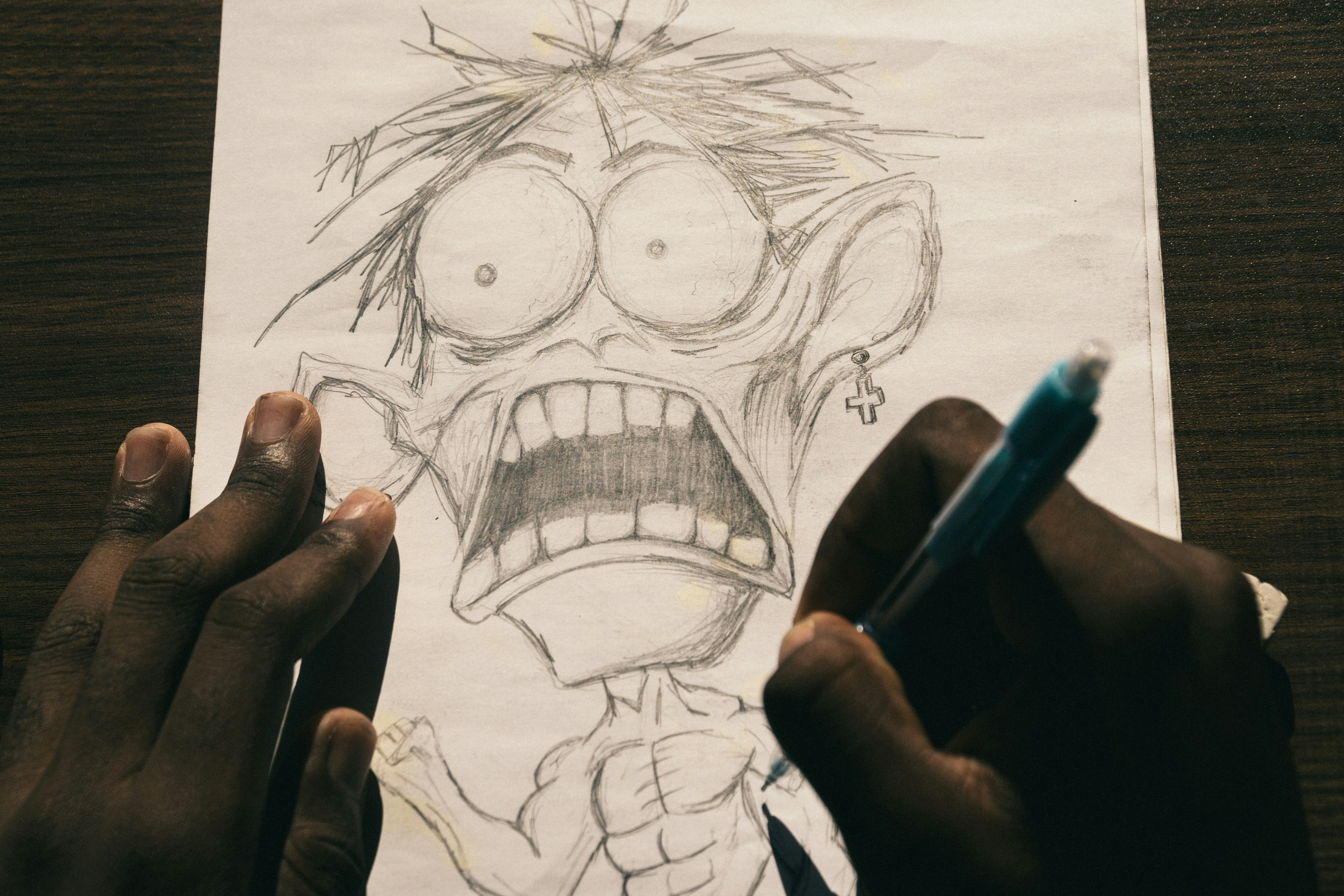 A person drawing a cartoon character with a wide-eyed expression on white paper.