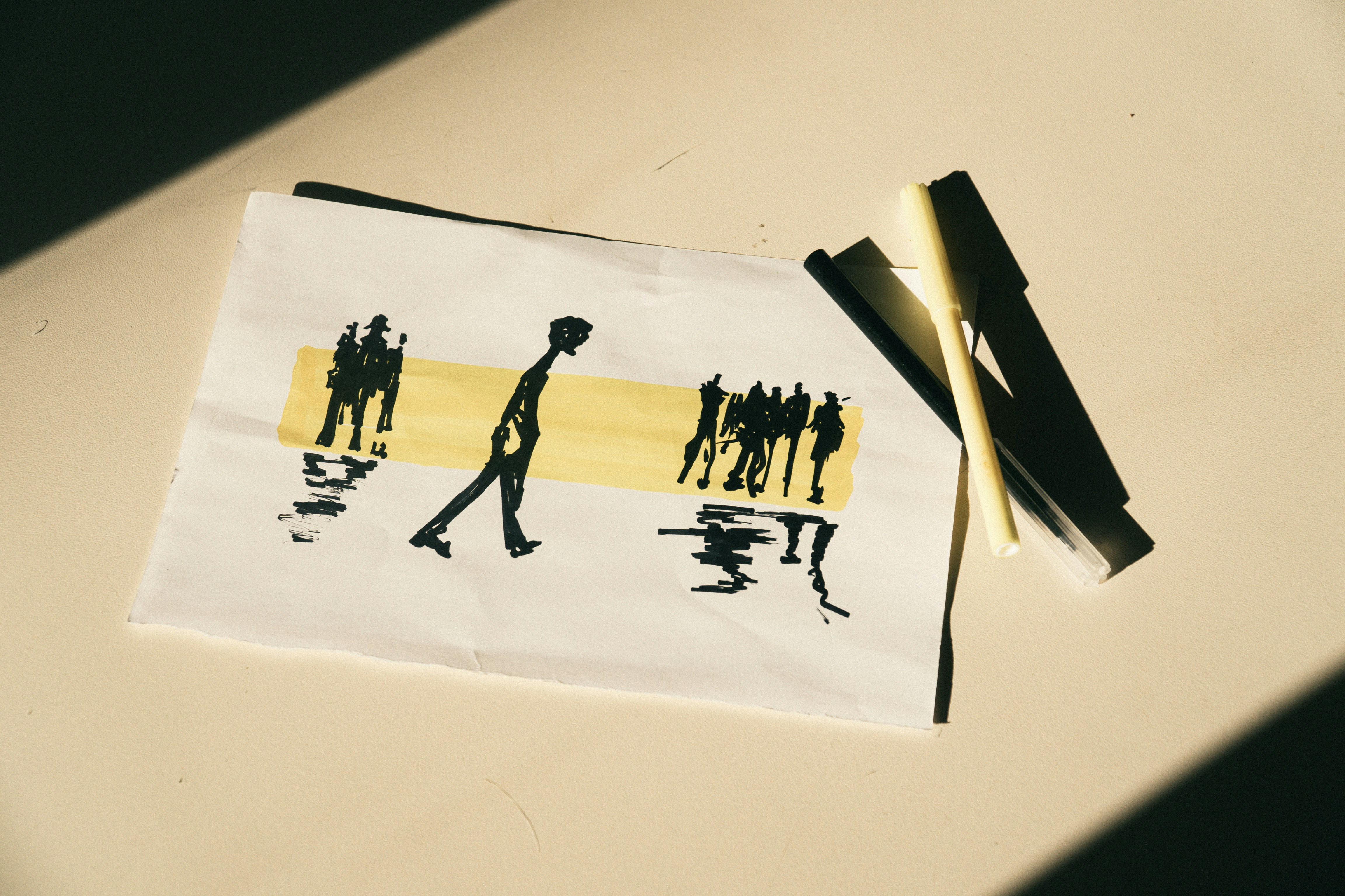 A sketch of people walking on a yellow stripe with two pens nearby.