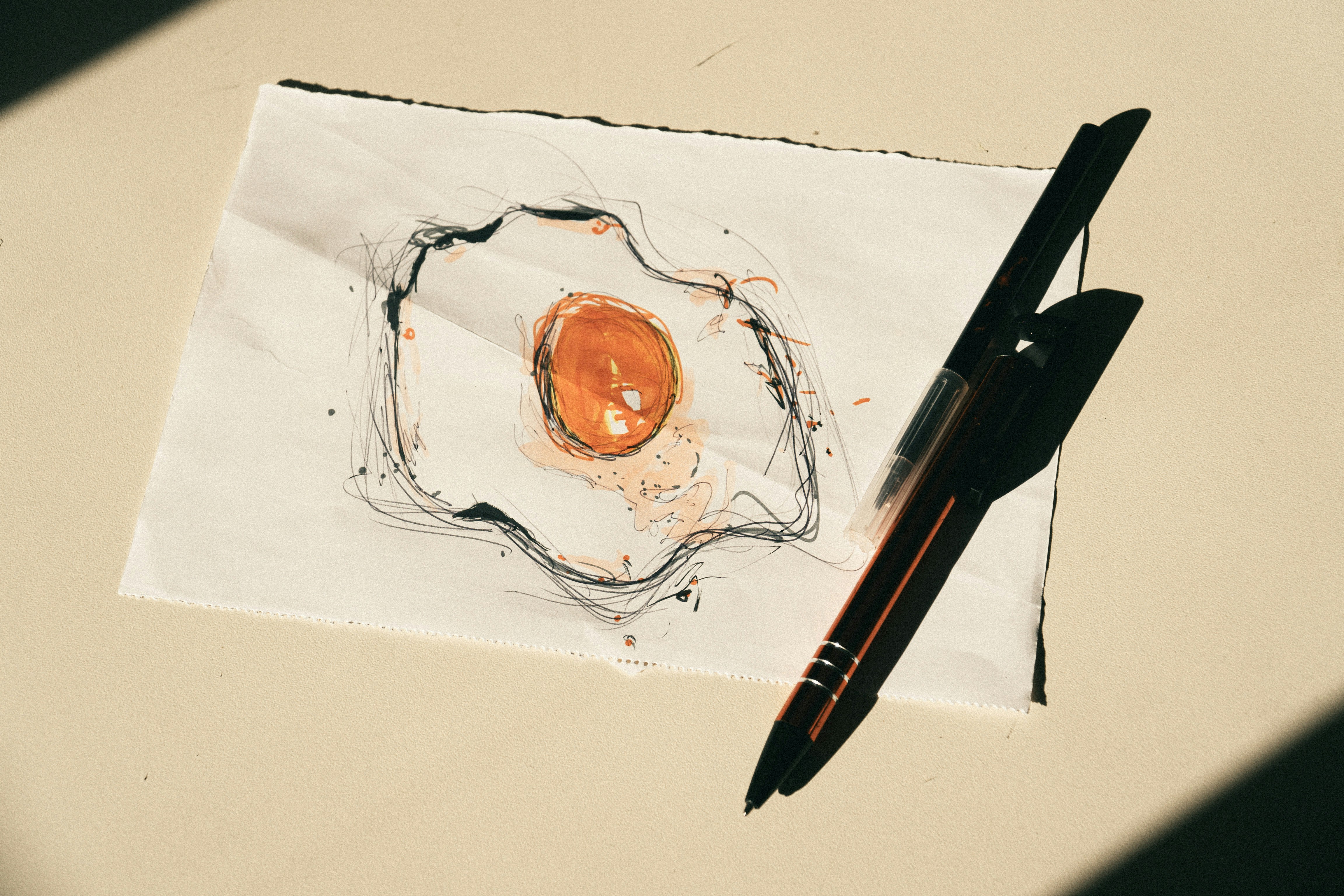 A sketch of a fried egg on paper beside a black pen.