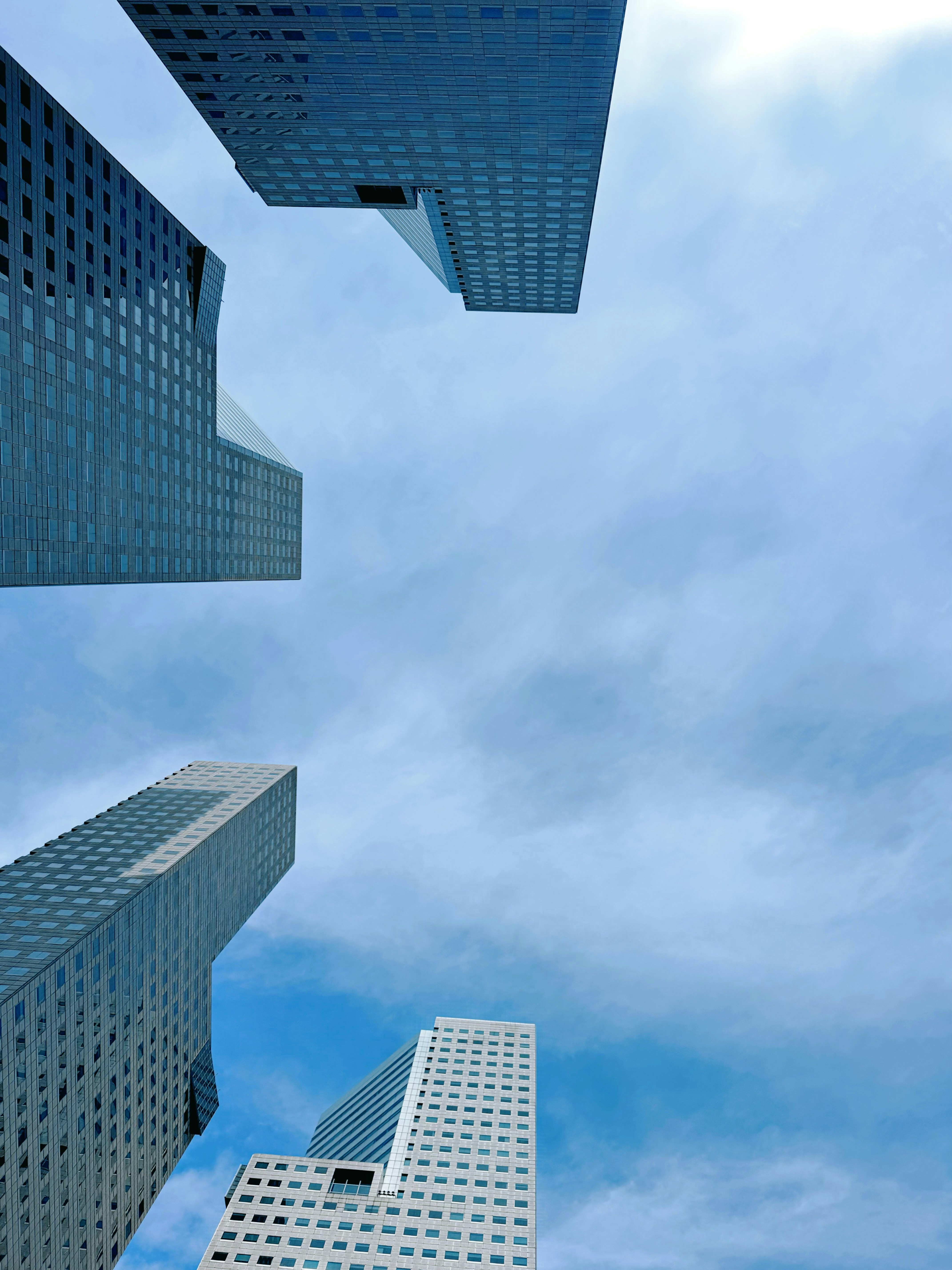 Low-angle view of four modern glass skyscrapers against a bright blue sky.