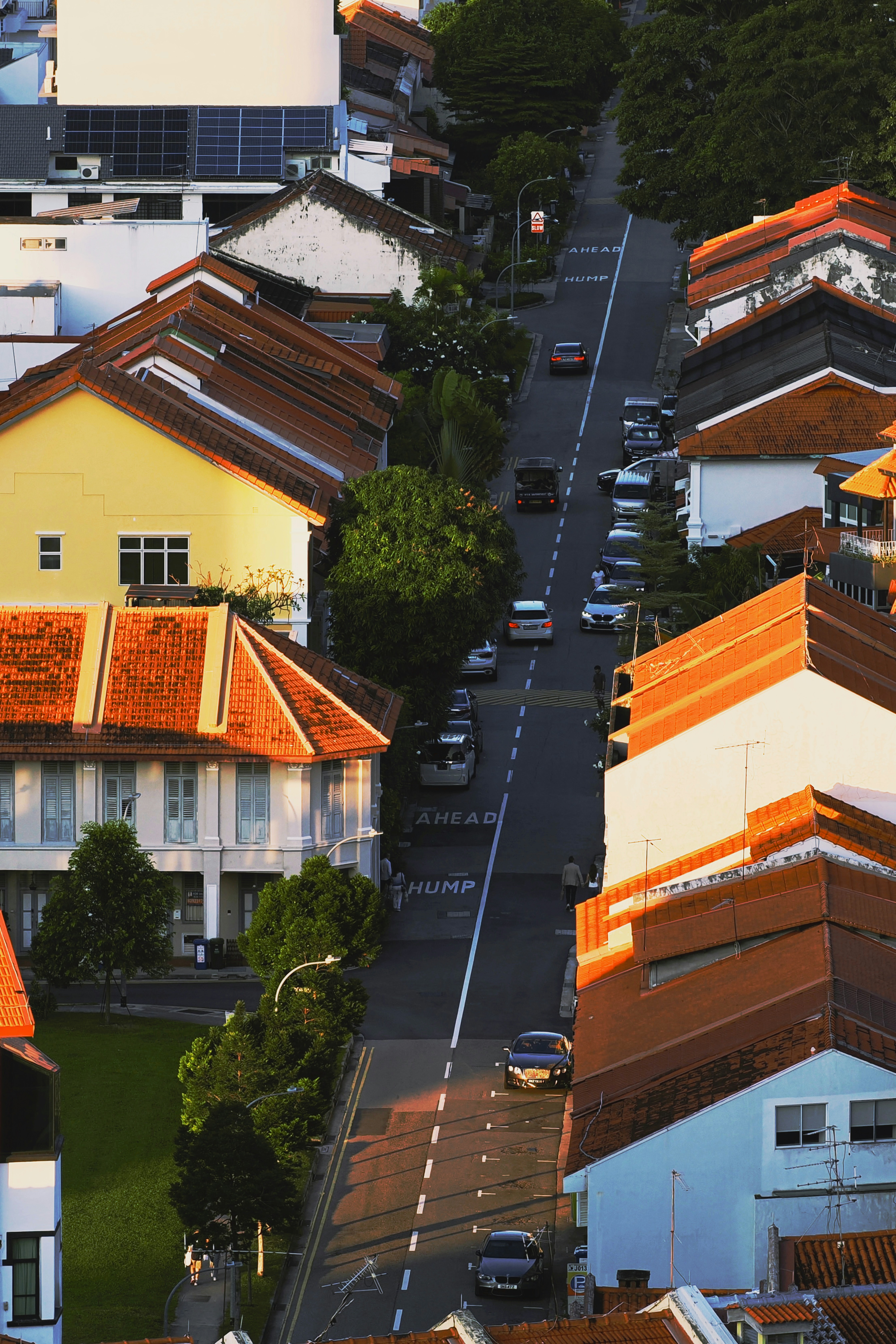 An aerial view of a street lined with shophouses and parked cars at golden hour.