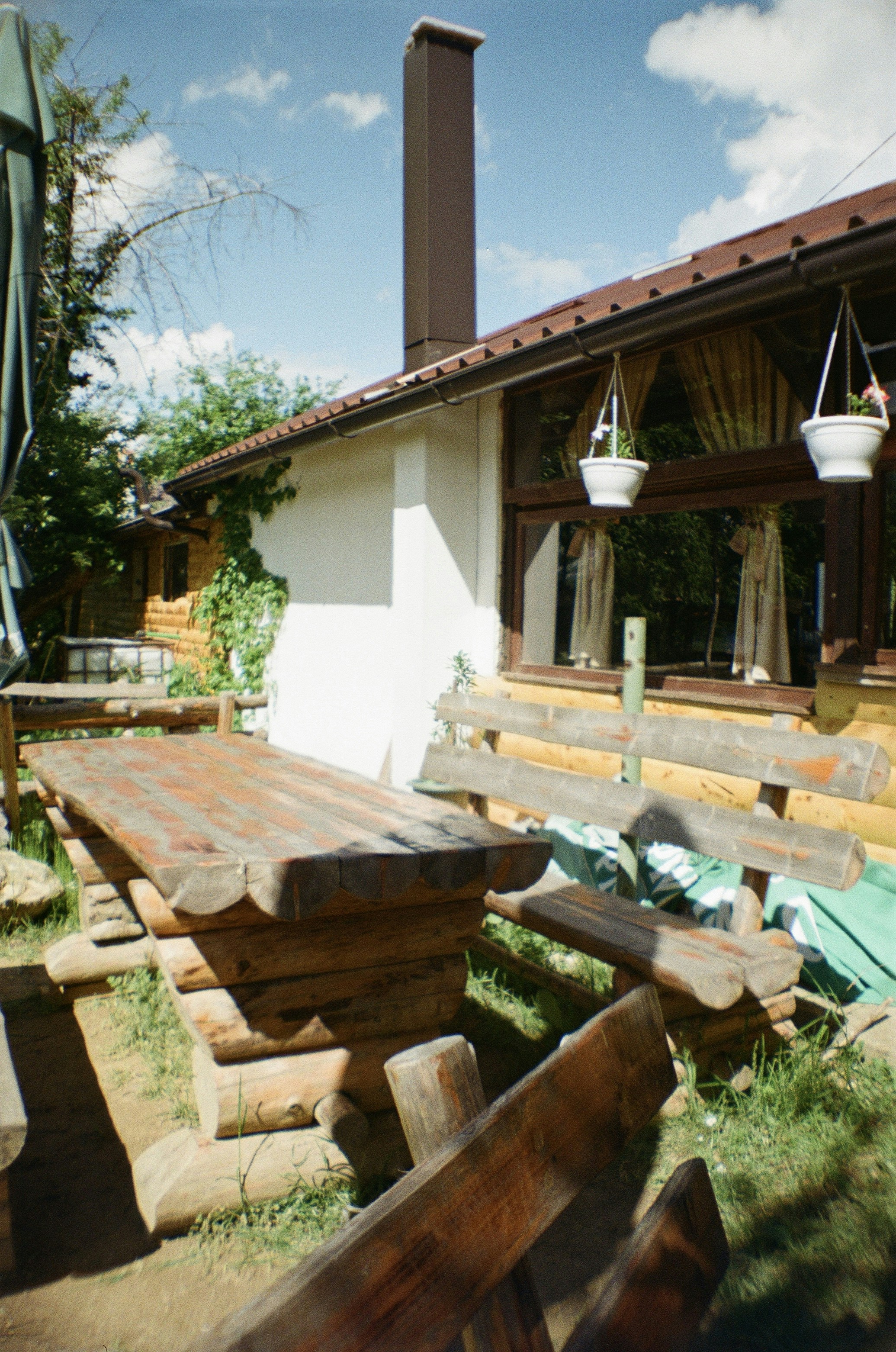 A rustic wooden table and bench set on a lawn beside a house