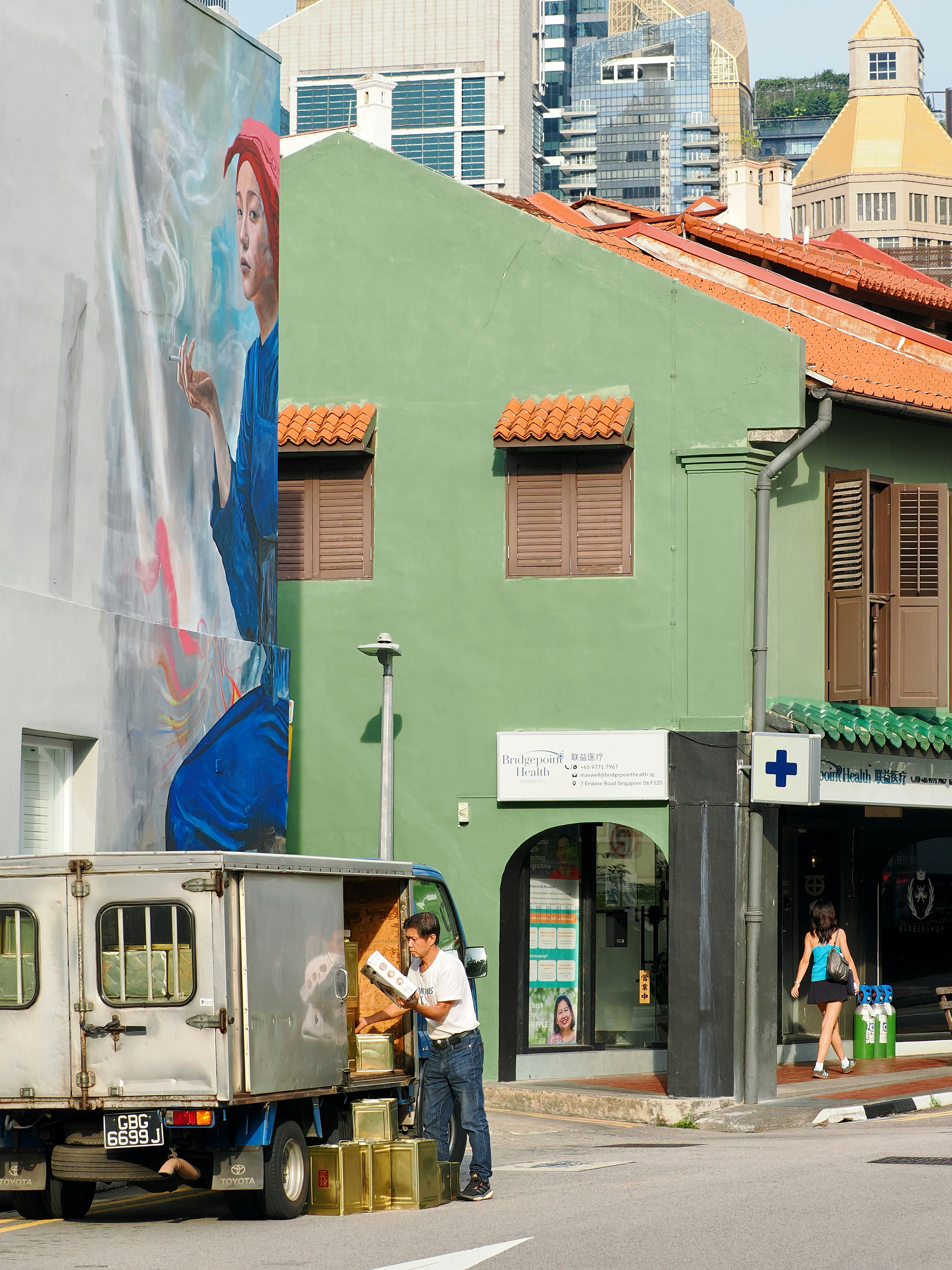 A man unloading metal containers from a truck near a green building in Singapore.