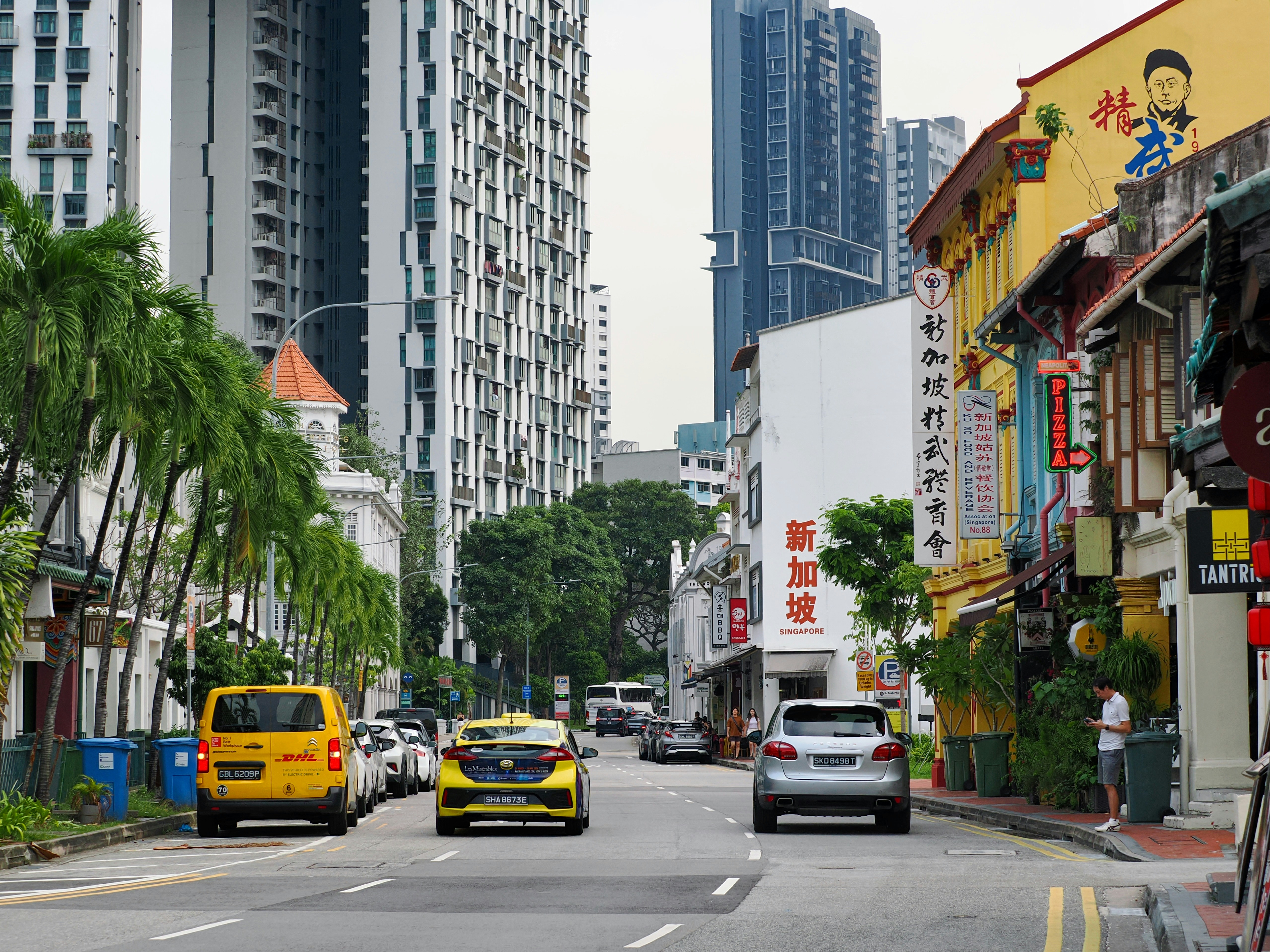Cars driving on a street in Singapore lined with historic shophouses and modern skyscrapers.