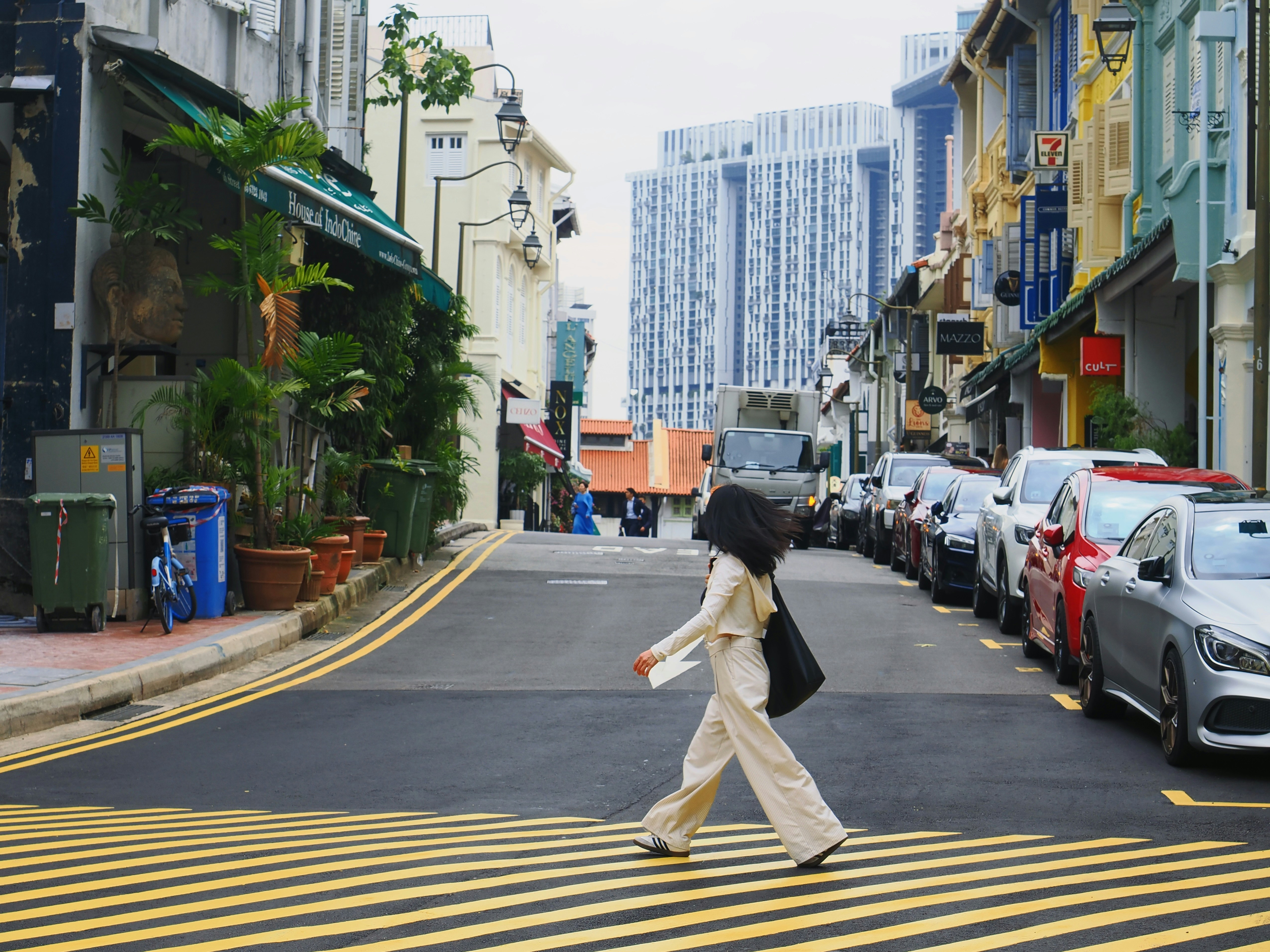 A person in a cream outfit walking across a yellow-striped crosswalk in Singapore.