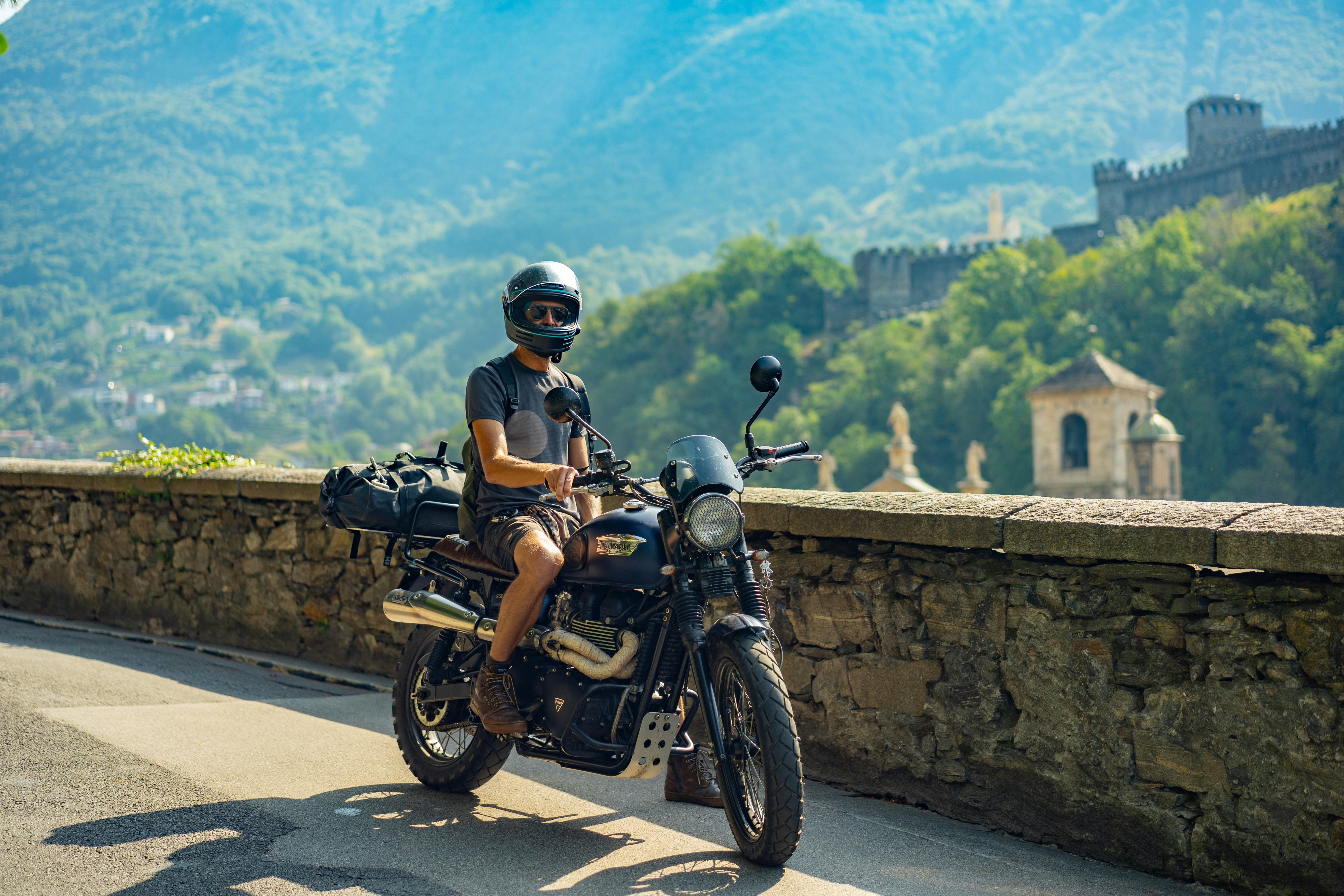 Uma pessoa de capacete em uma motocicleta ao lado de um muro de pedra em Bellinzona.