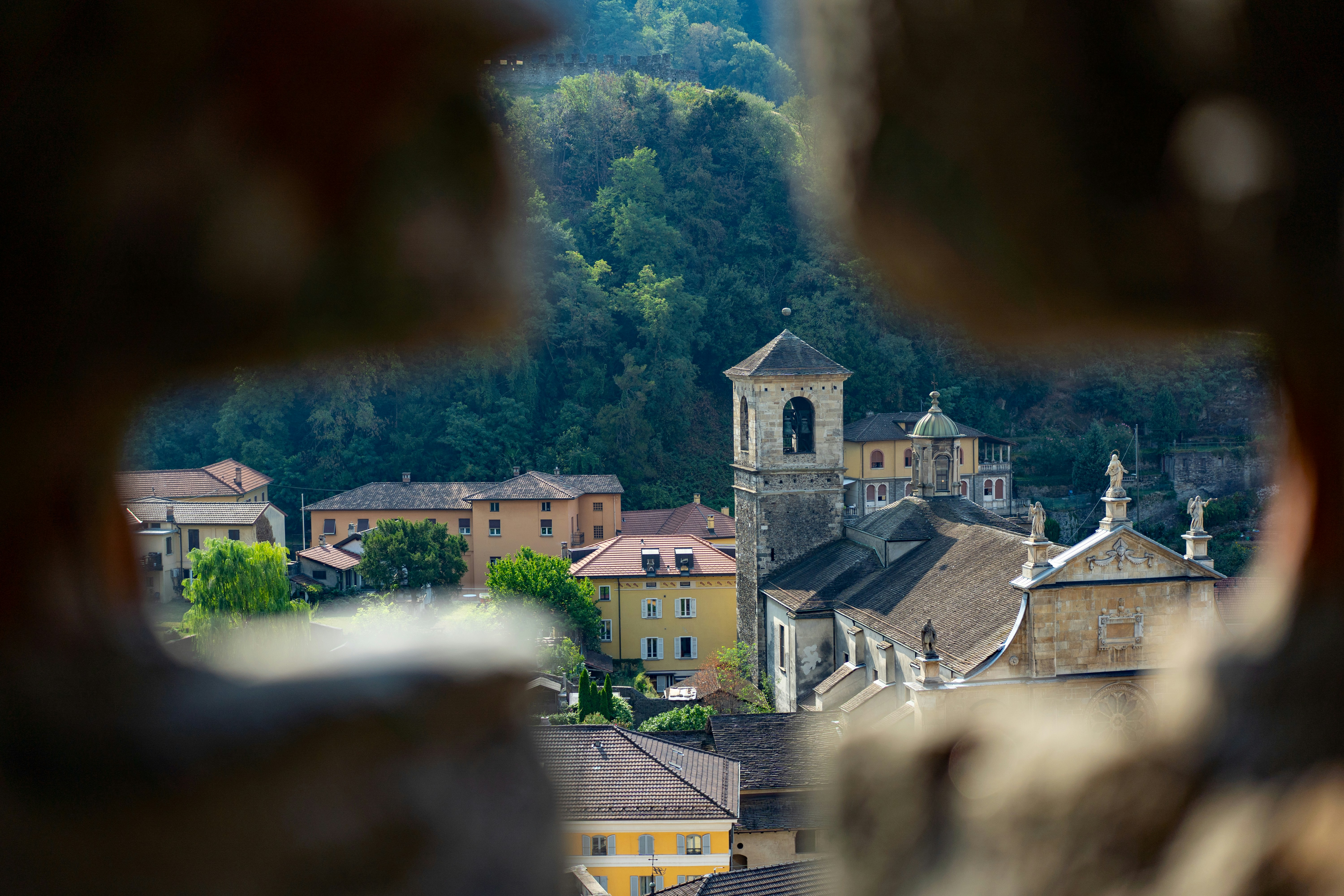 Vista de uma igreja e prédios da vila emoldurados por um muro de pedra.