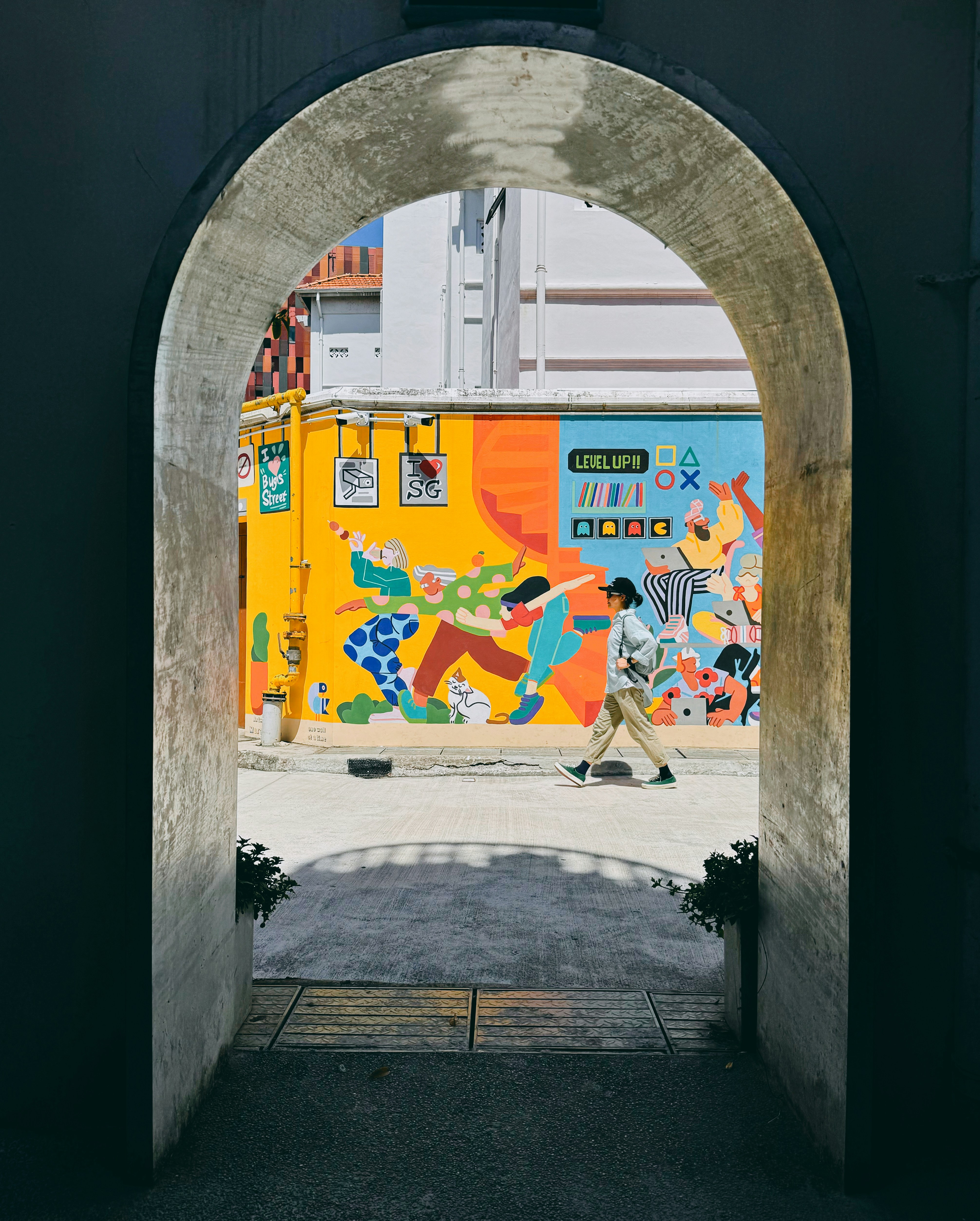 A person walking past a vibrant yellow mural in a narrow alleyway.